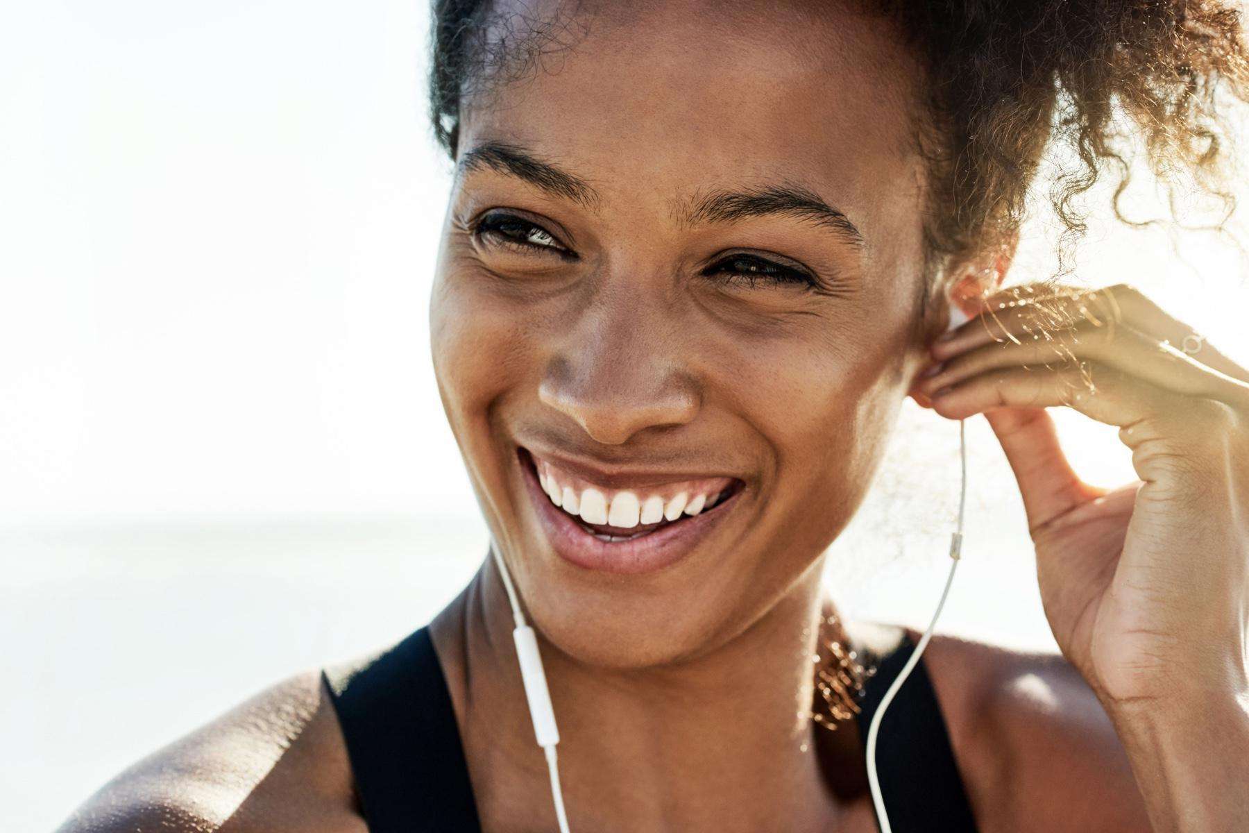 A close-up of a young woman's face as she is putting her headphones into her ears.