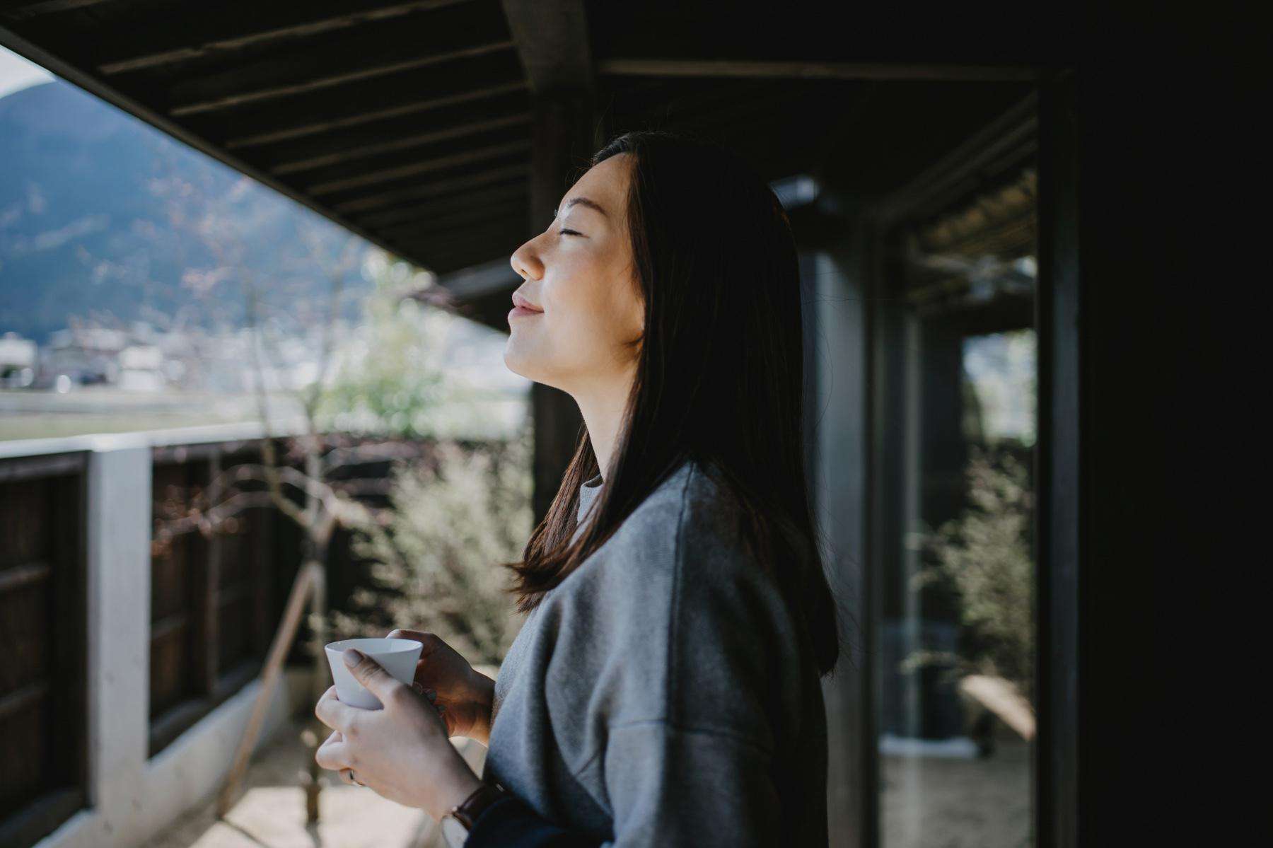 Woman holding a coffee cup on her balcony as she is breathing in the fresh air.