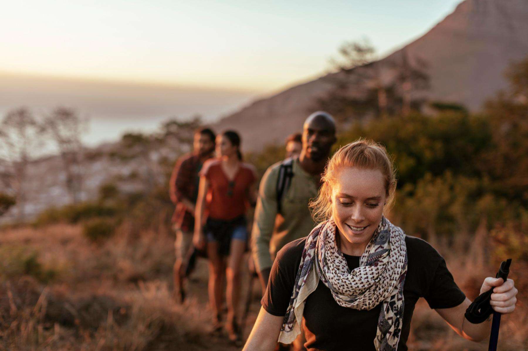 Red-haired woman leading a group of three men and two women on a hike up a mountain during sunset.