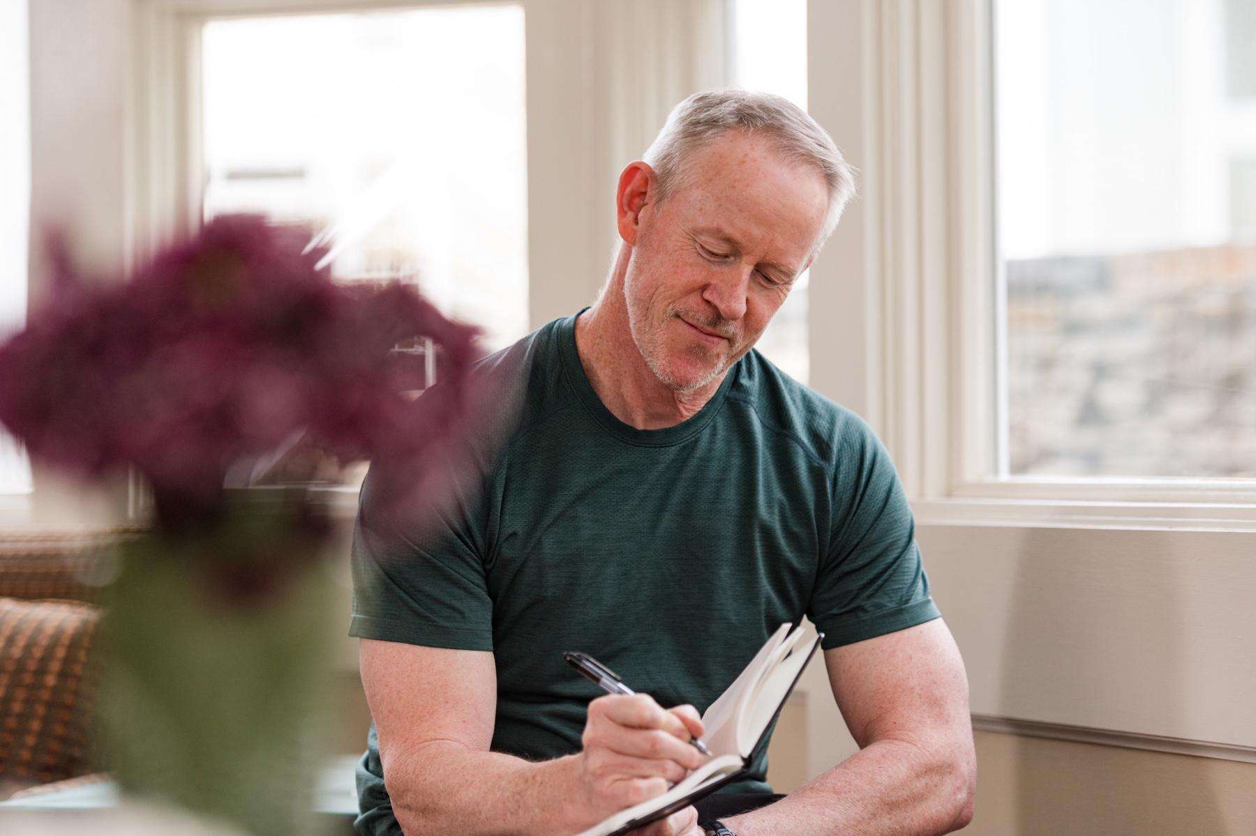 Man writing in his journal next to a window.