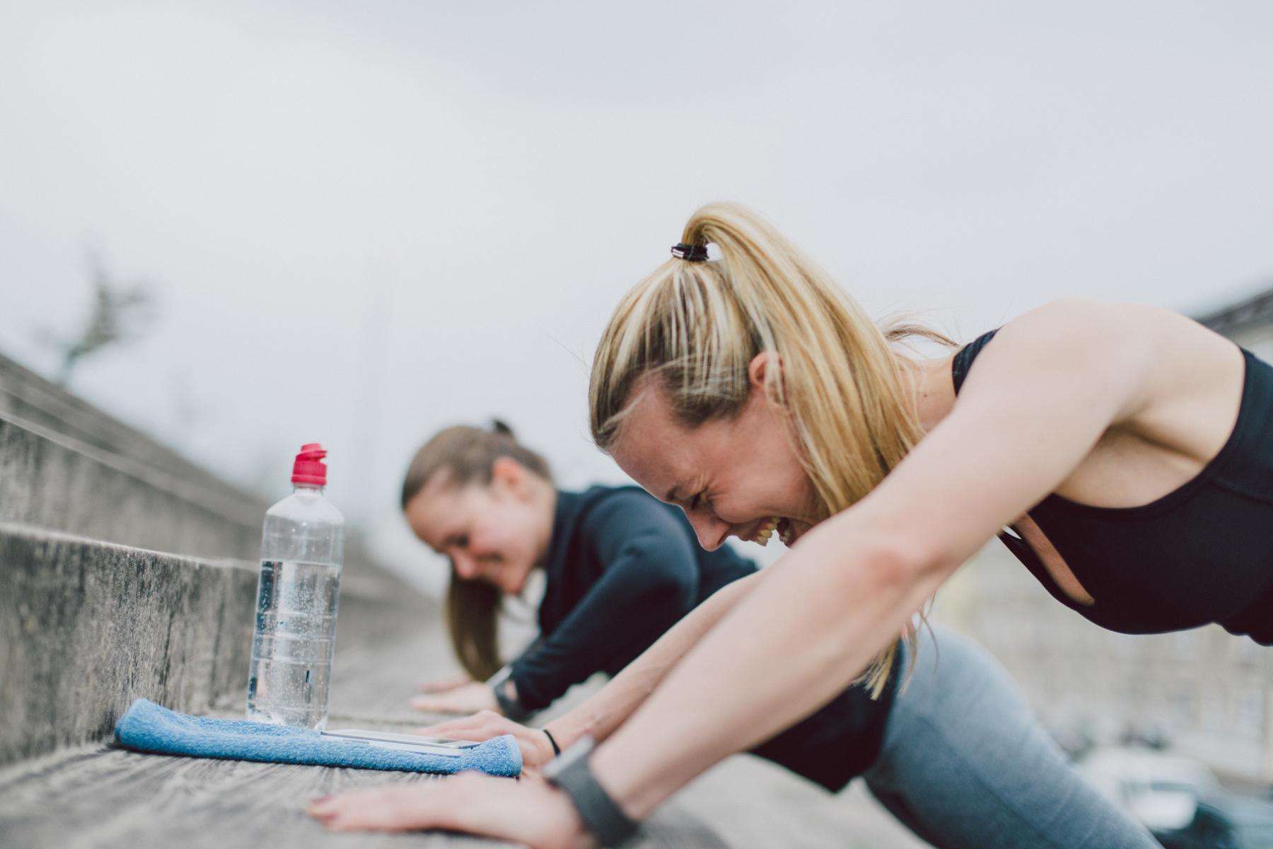 two women laughing while doing push-ups on cement steps outside