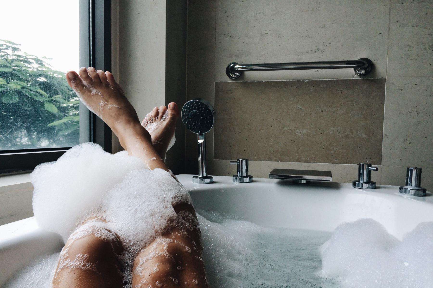 A woman's legs and feet sticking out of a bathtub with bubbles.