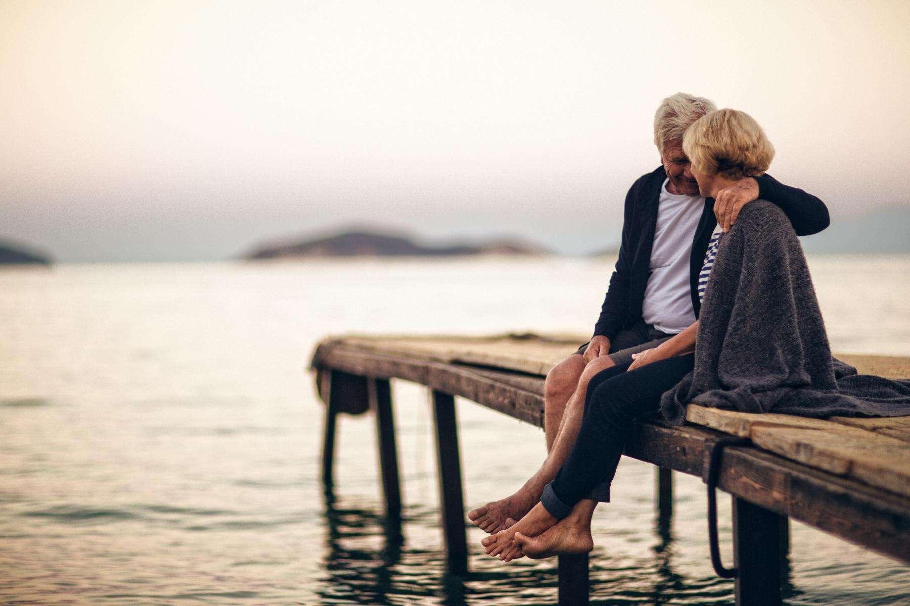 A mature couple sitting on a dock together.