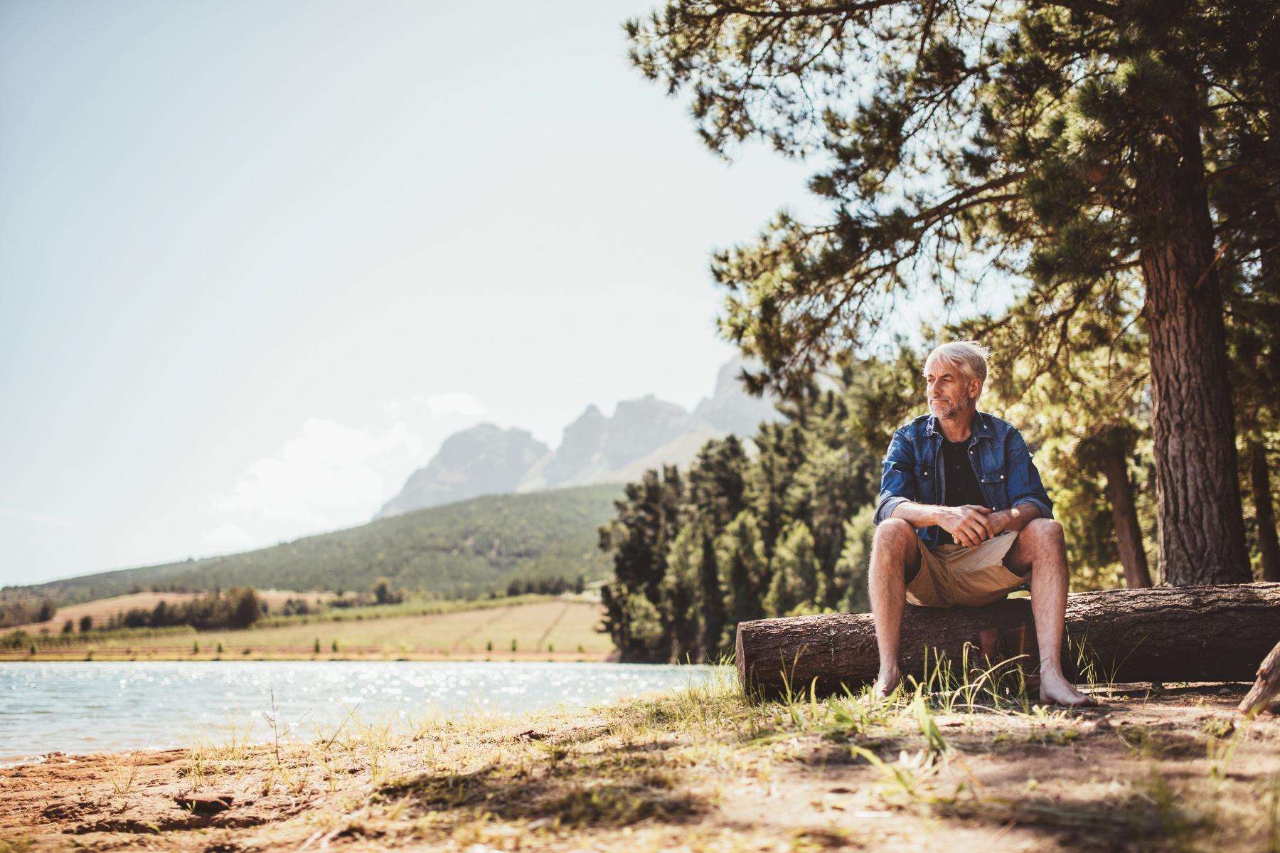 Mature man sitting near a lake looking out into the distance.