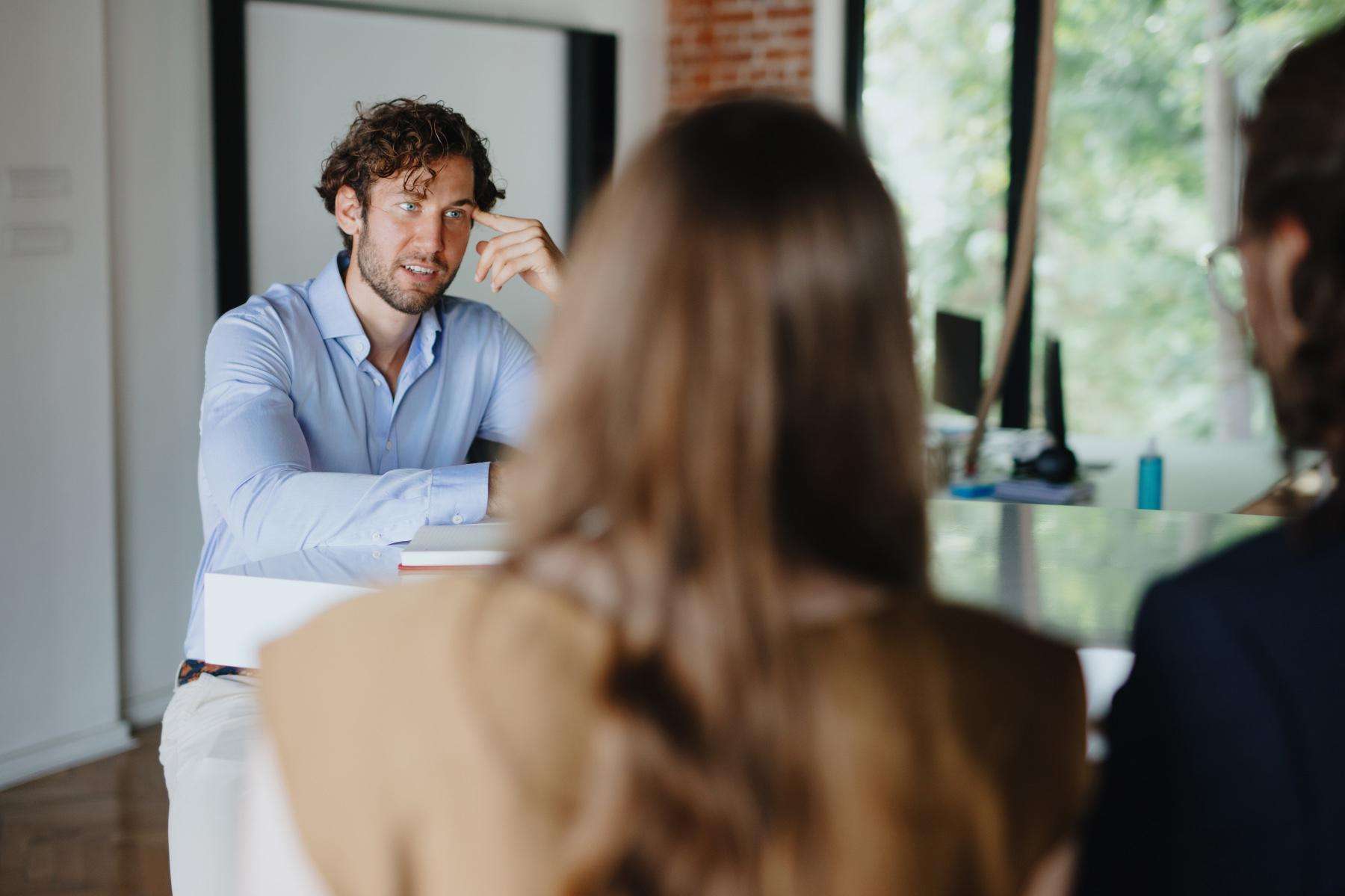 A young man speaking with two female coworkers.