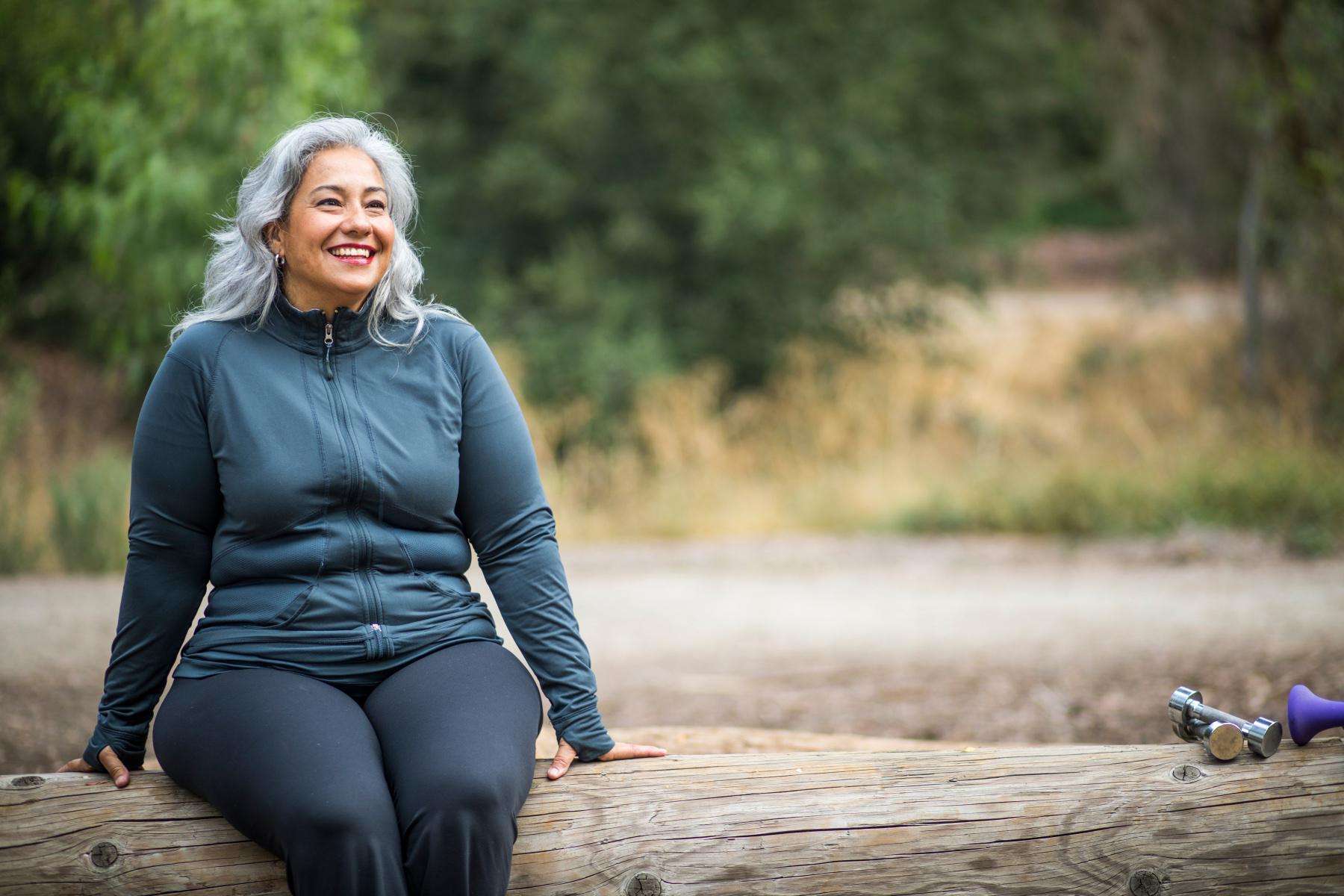 Woman smiling and looking forward while sitting on a log outside.