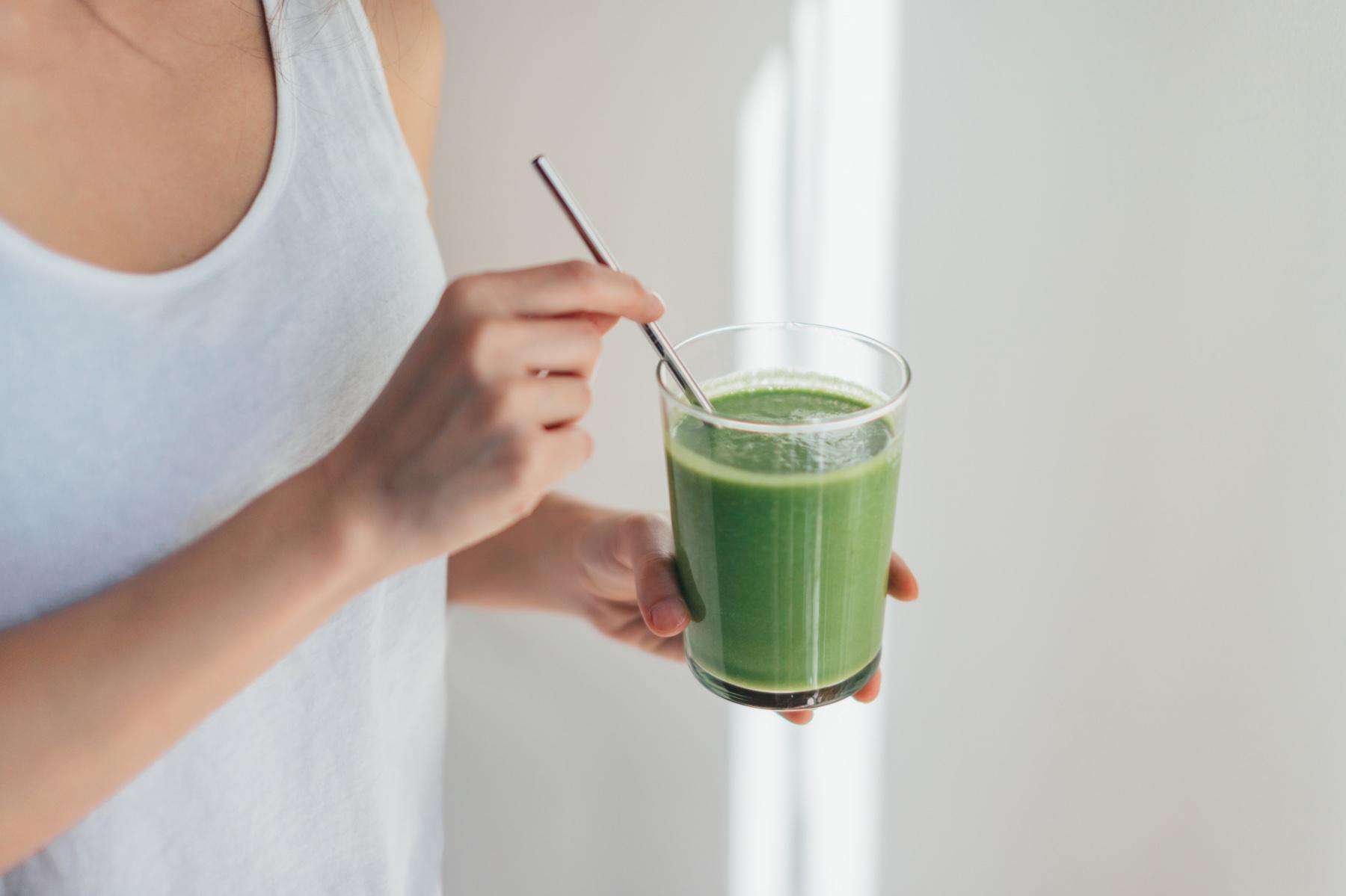 Woman drinking green smoothie in glass with metal straw.