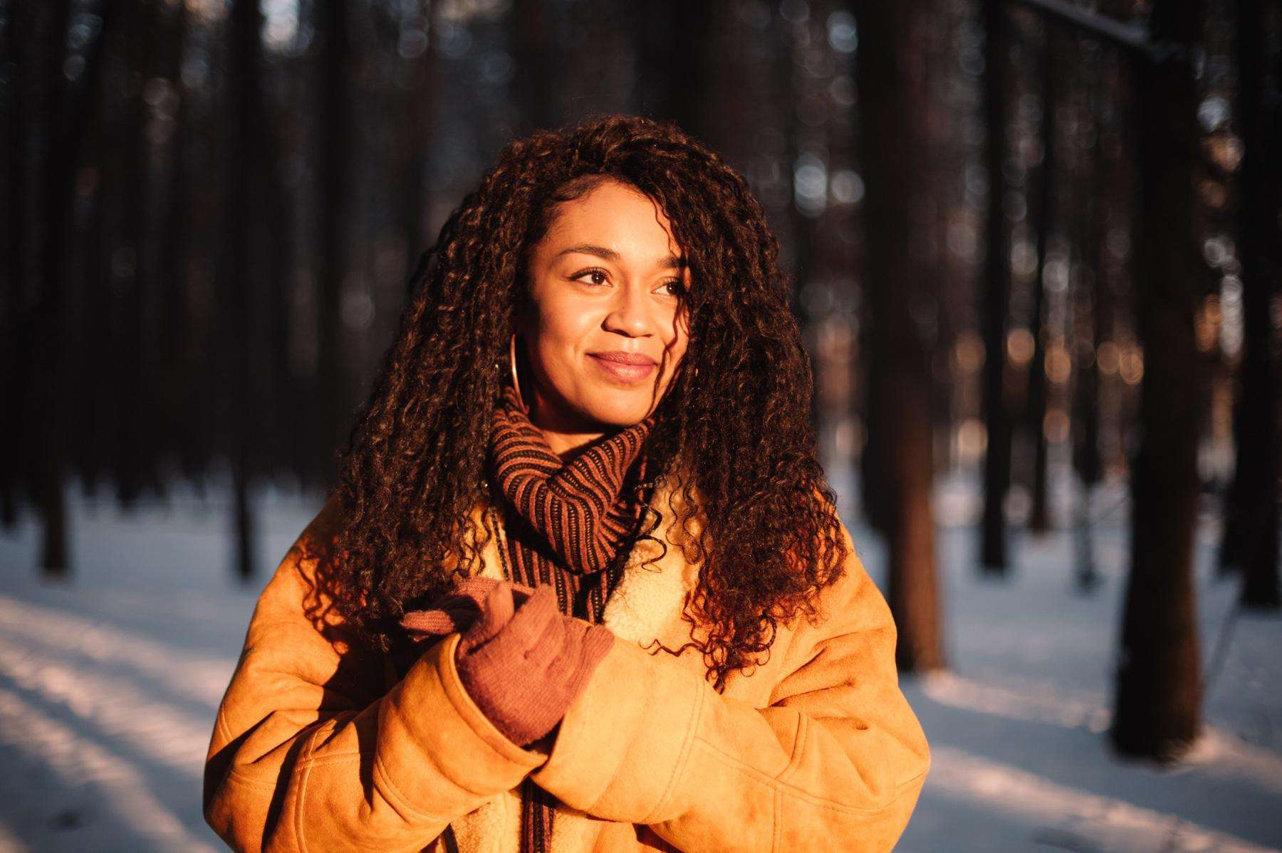 A young woman with curly hair standing in a snow-covered forest.