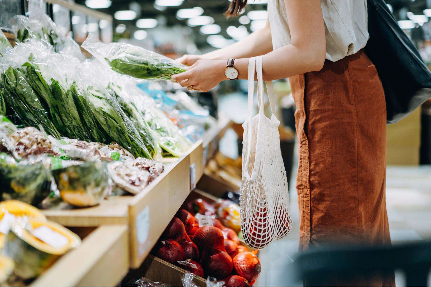sideview of woman from neck down shopping in the produce section of a grocery store