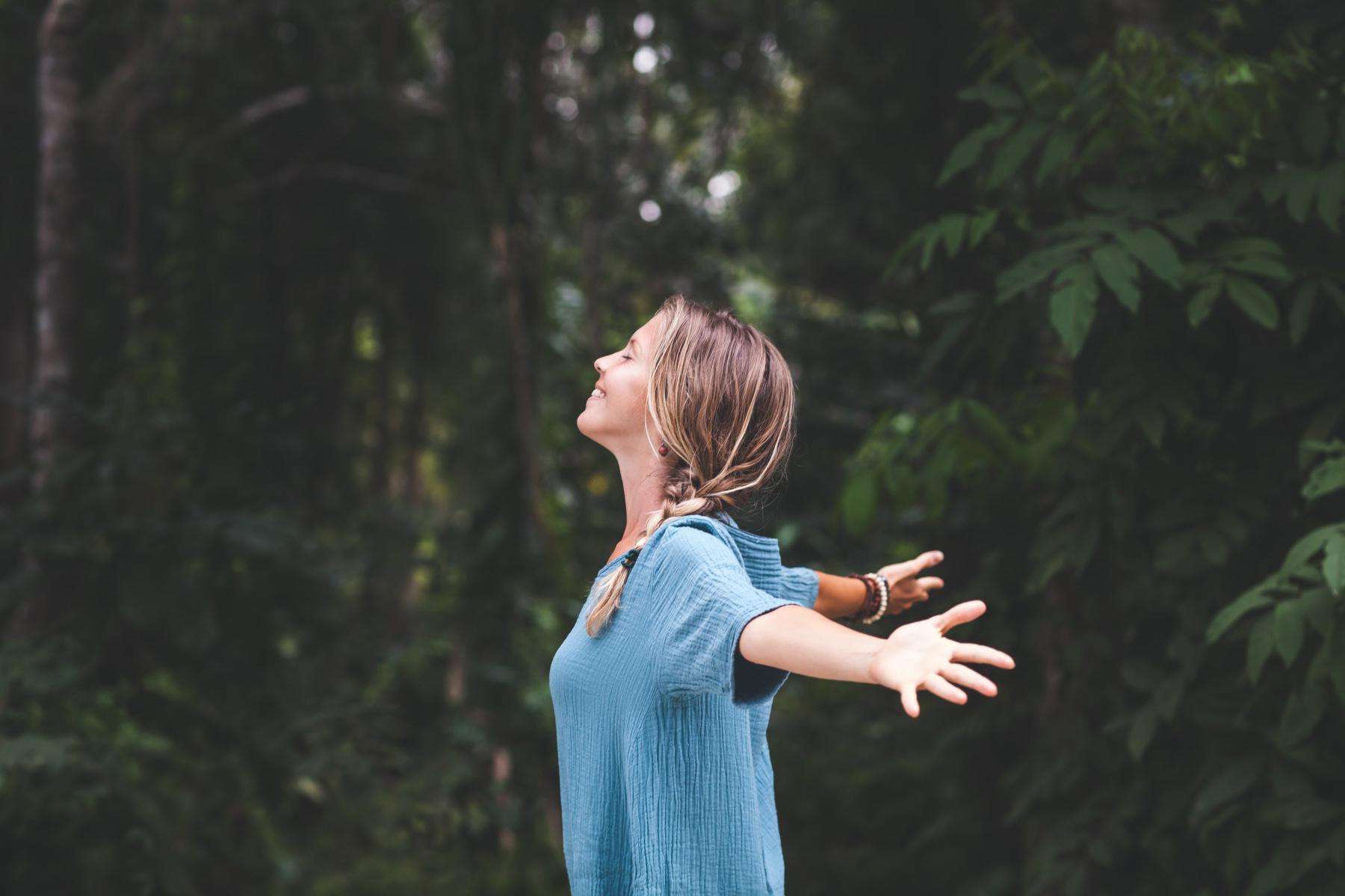 Woman standing in the forest and looking up at the sky.