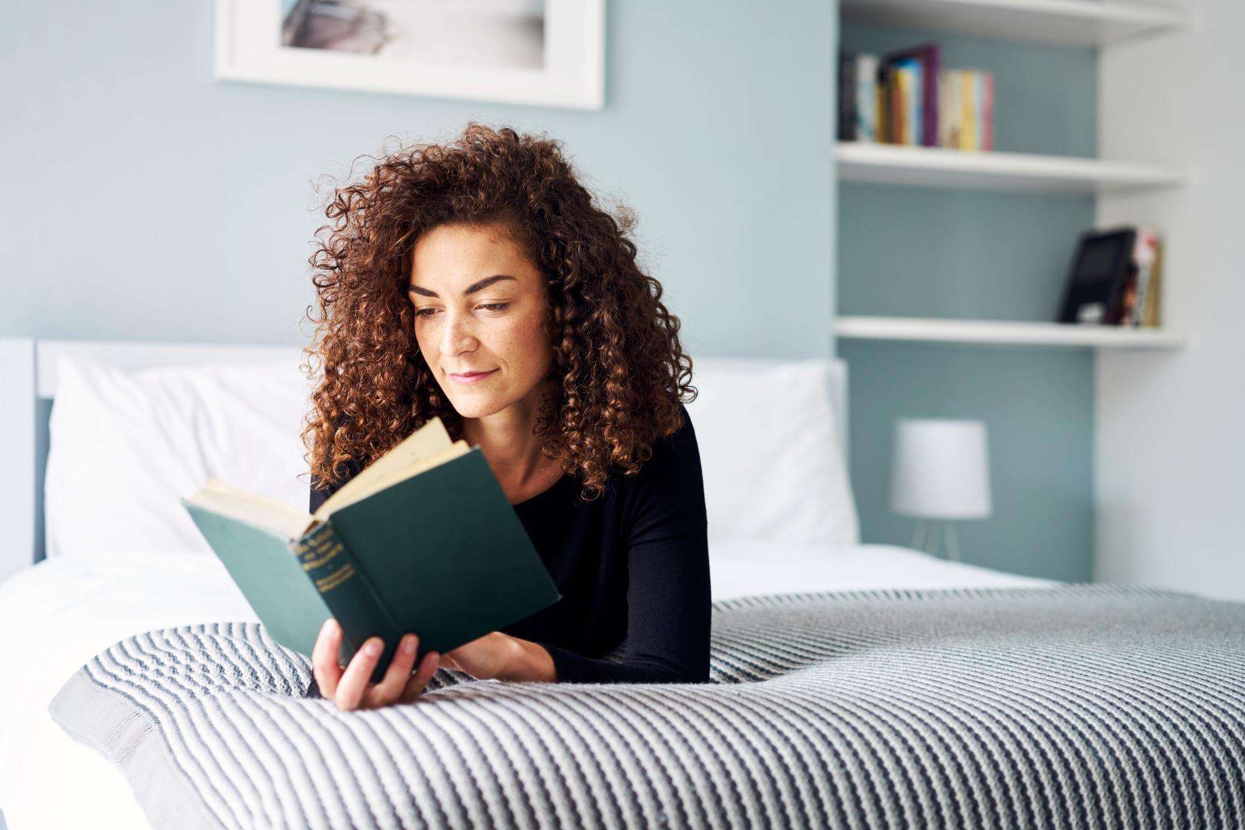 Woman laying on her bed reading a book.