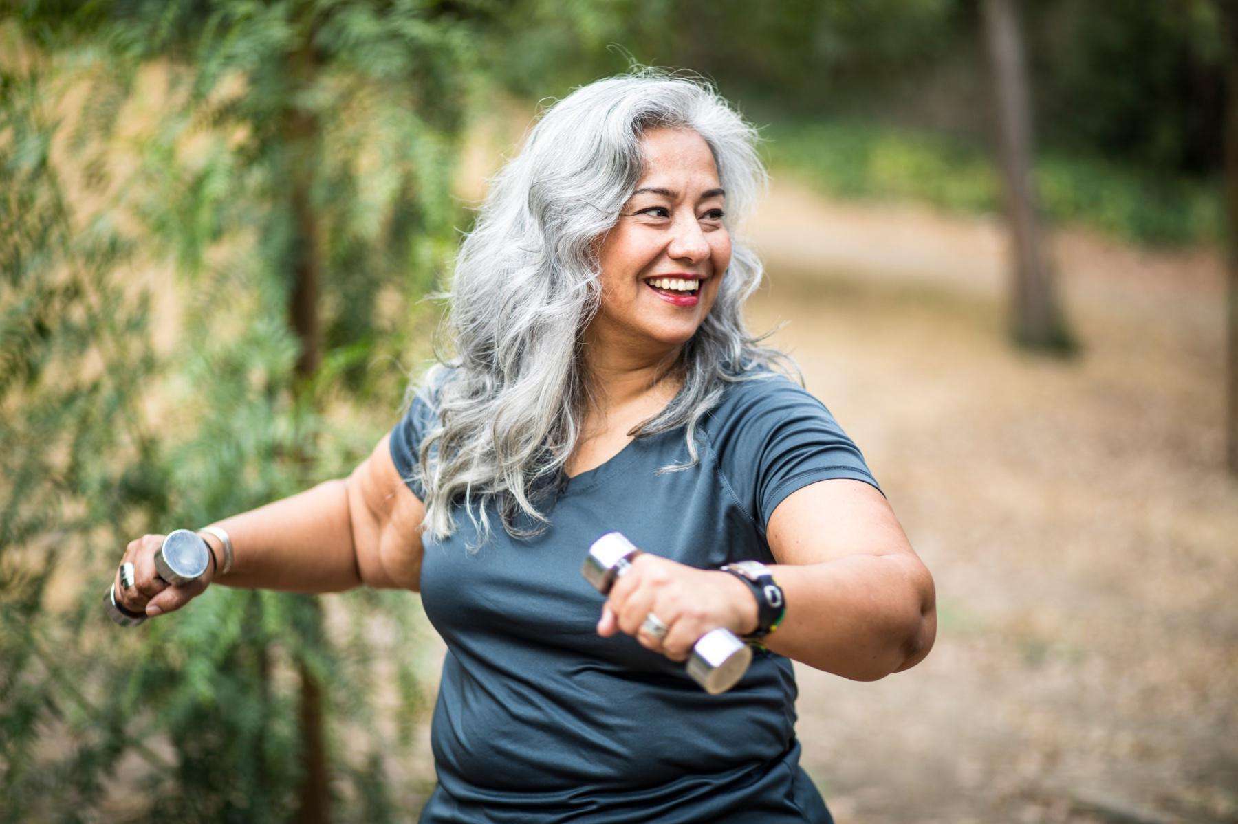 woman outside doing a twist with small silver dumbbells in her hands
