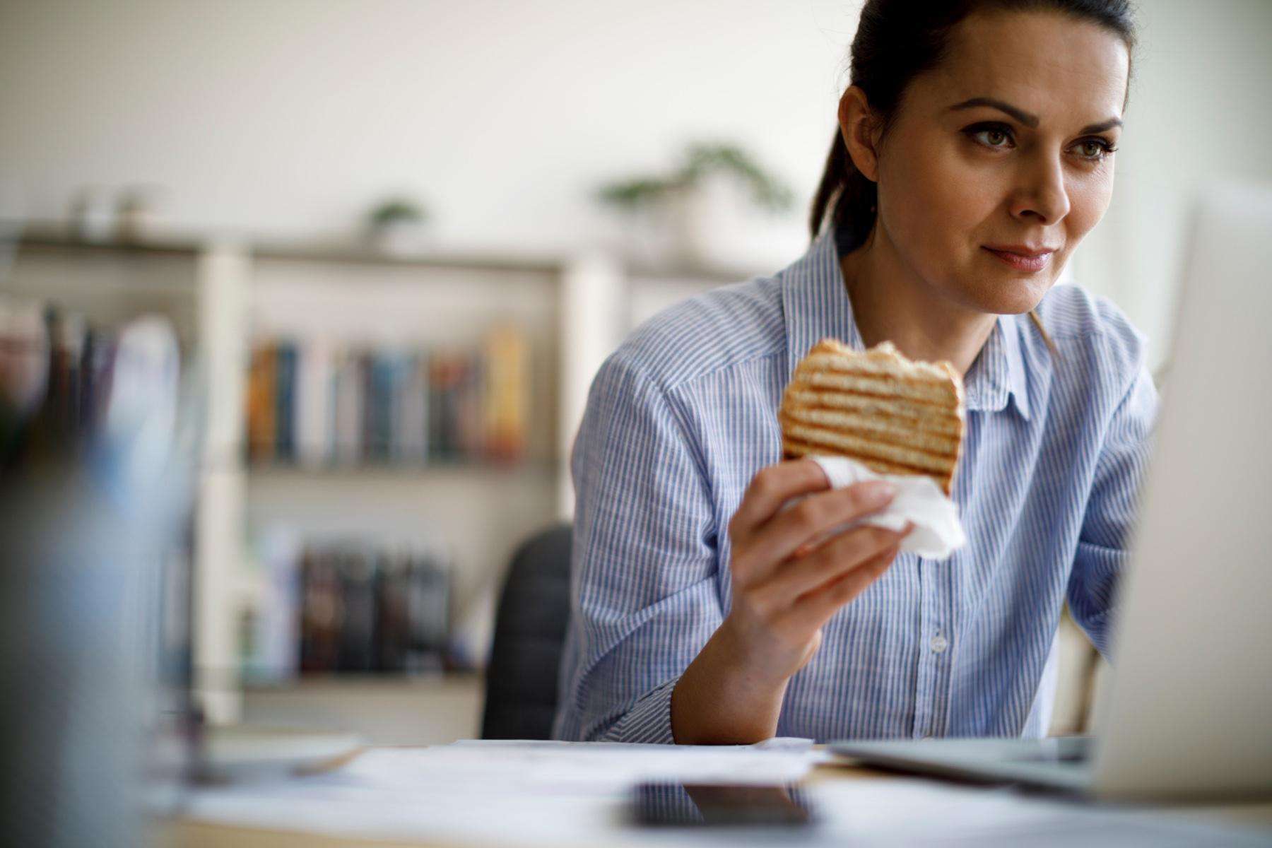 woman eating sandwich while working on laptop