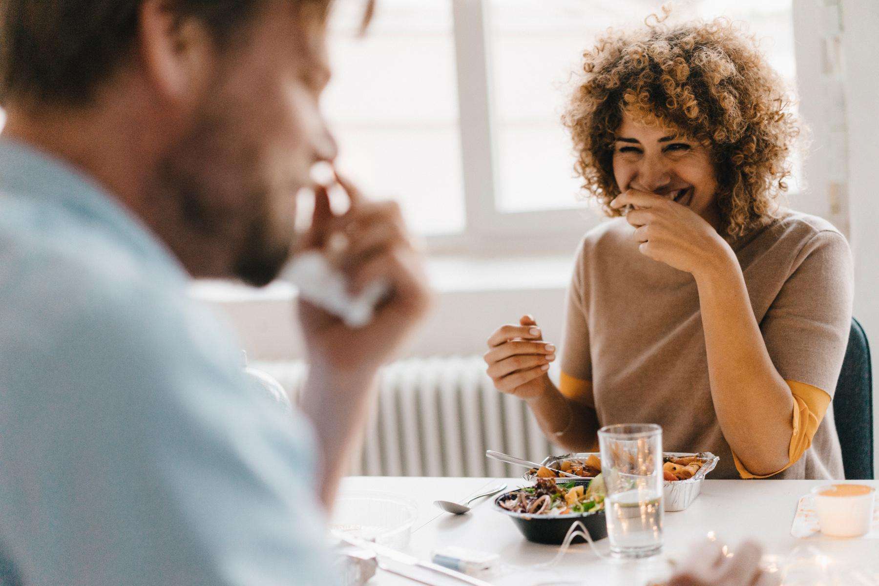 A couple laughing with each other while eating lunch.