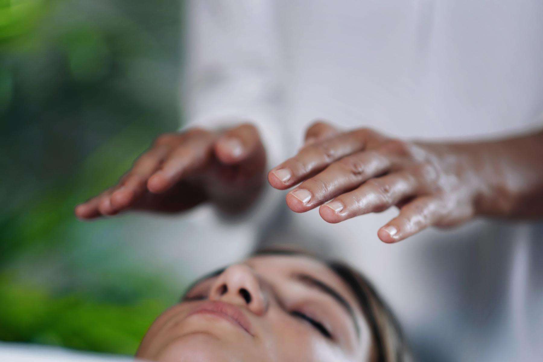 close-up of hands hovering above woman's face during a healing energy treatment