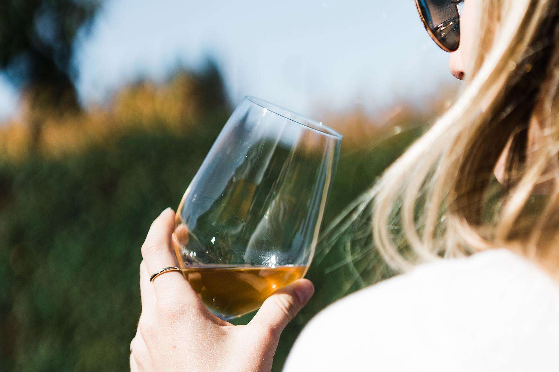 Close up of the back of a blonde woman's head as she holds a glass of white wine.