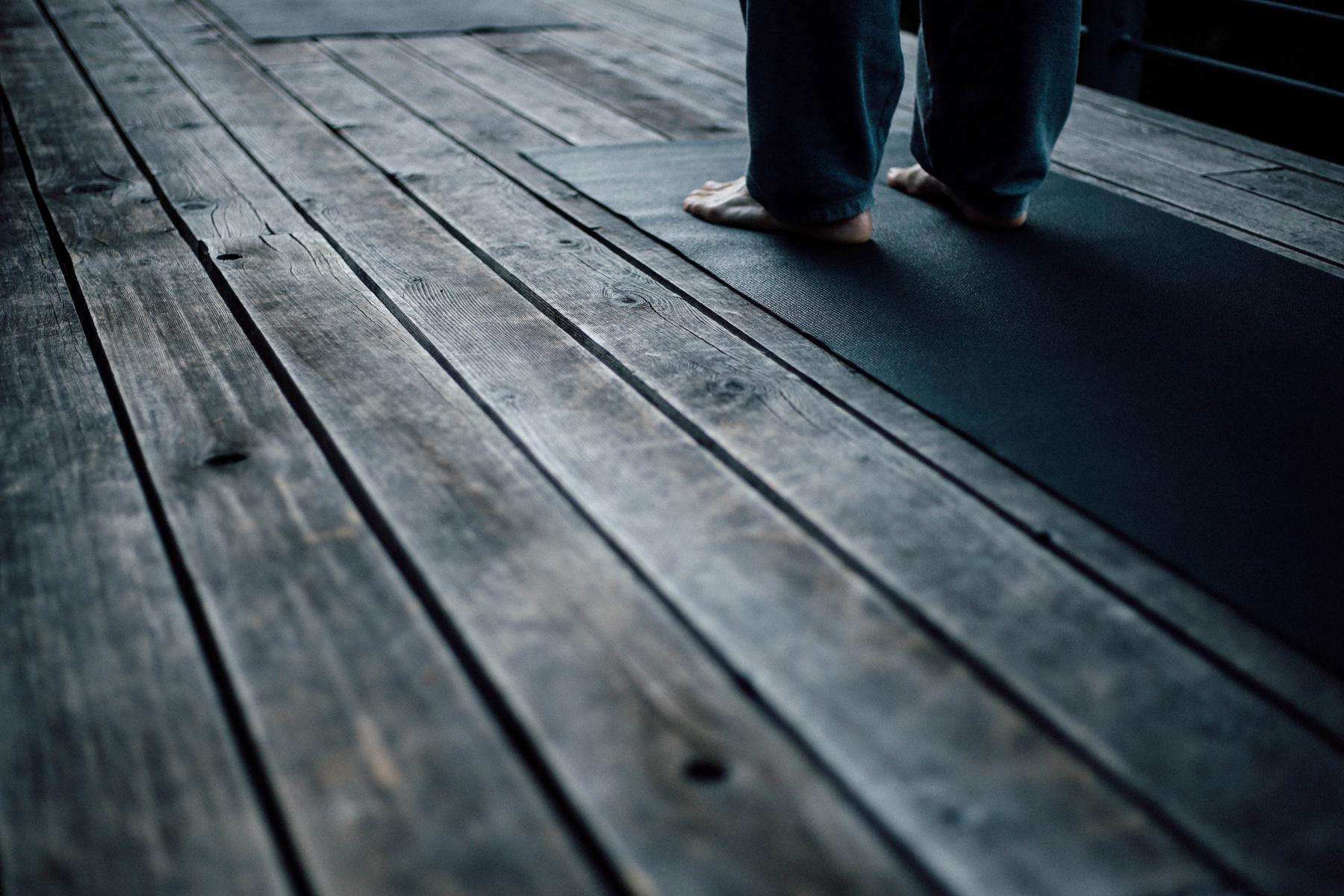 close-up of feet standing on yoga mat on wooden deck