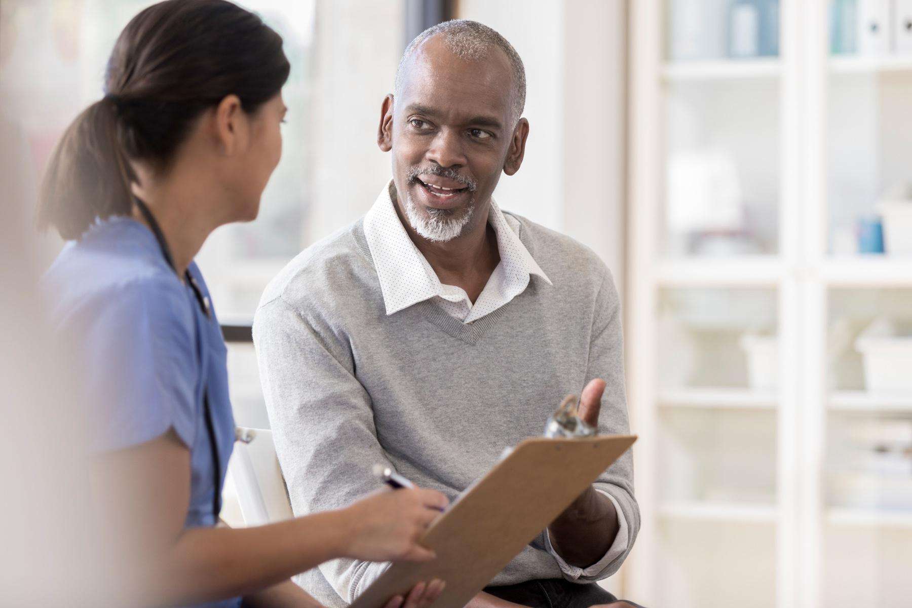 Older man having a conversation with a doctor about results on clipboard in front of them.