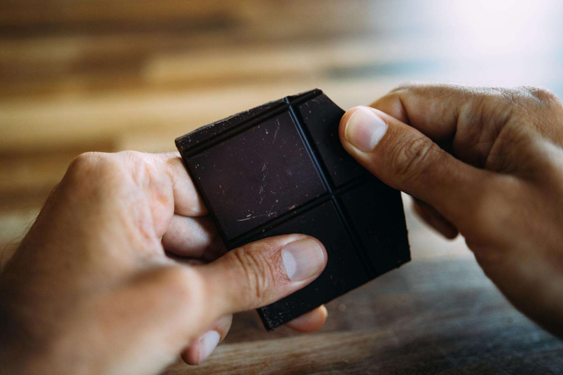 Close-up of man breaking apart bar of dark chocolate.