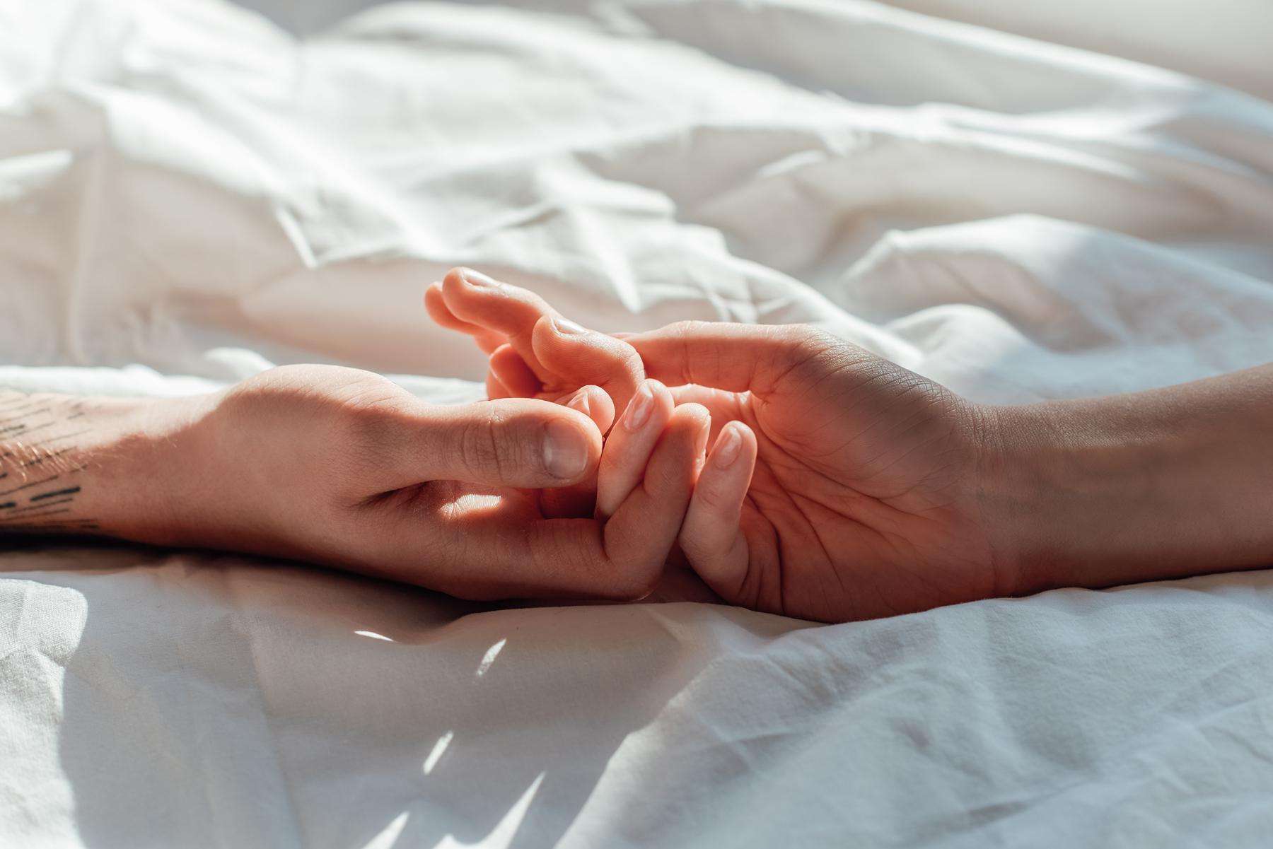 two hands touching on a bed