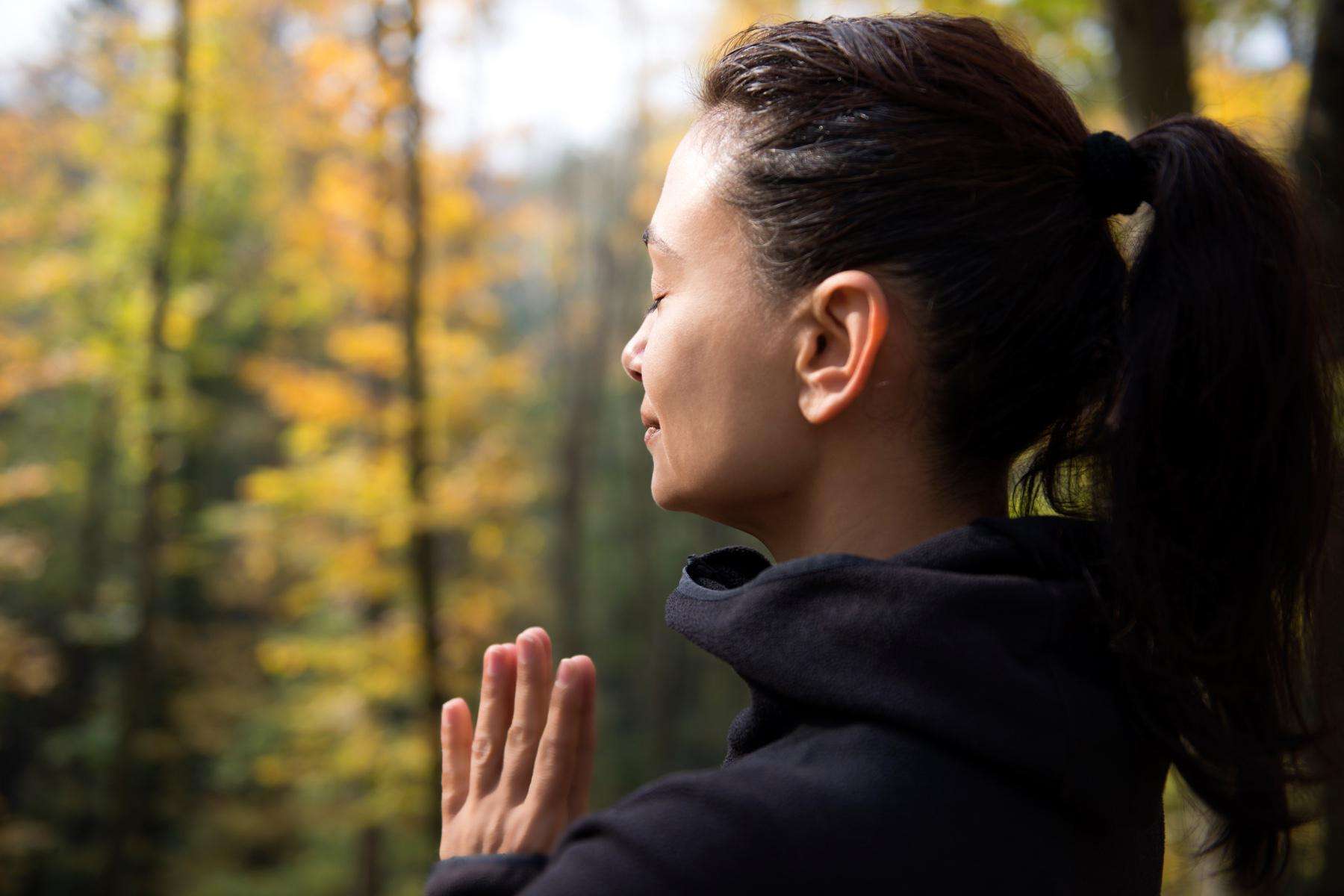 A brunette-haired woman meditating in an autumn-colored forest.