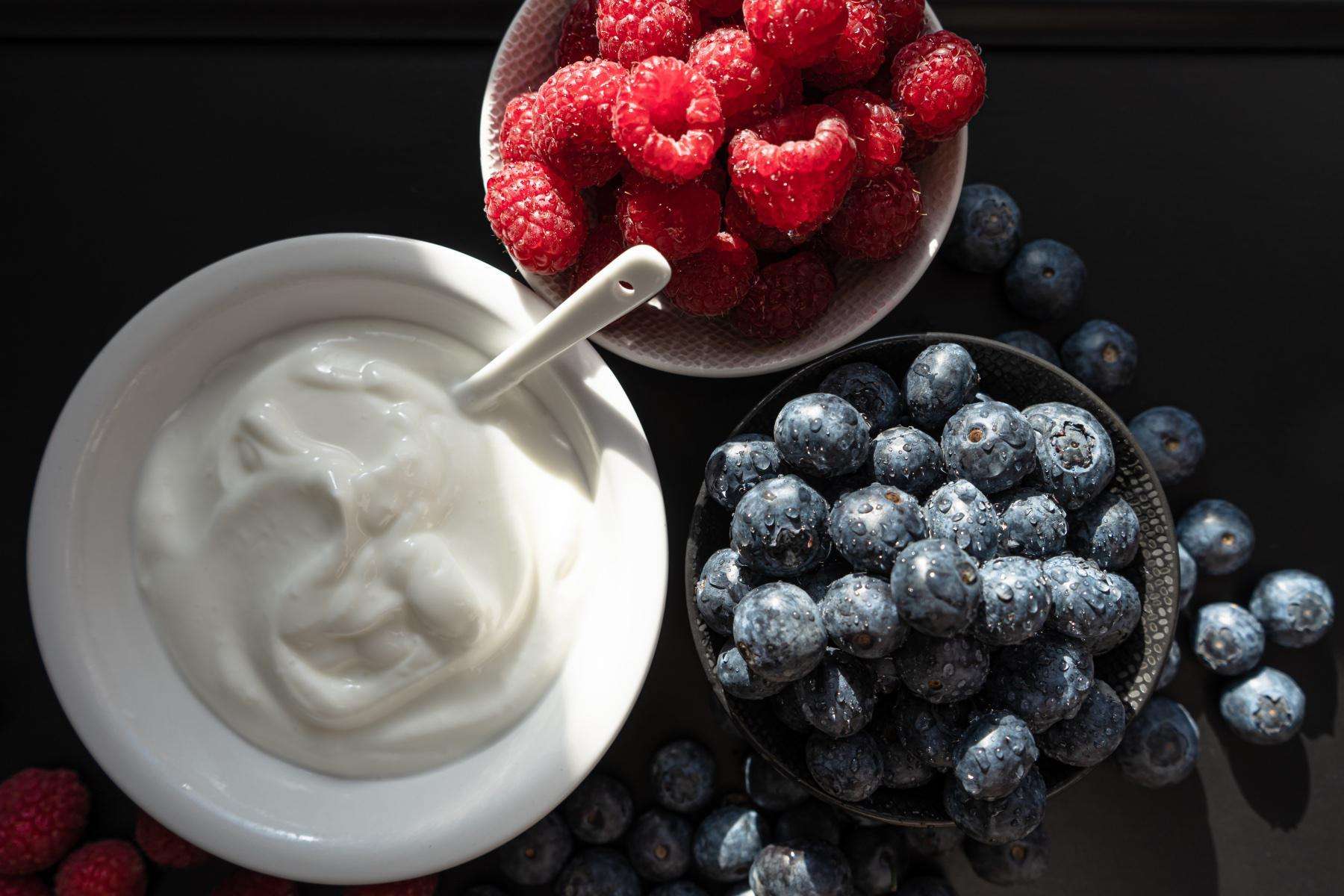 Close-up overhead shot of a bowl of yogurt next to a bowl of raspberries and a bowl of blueberries.