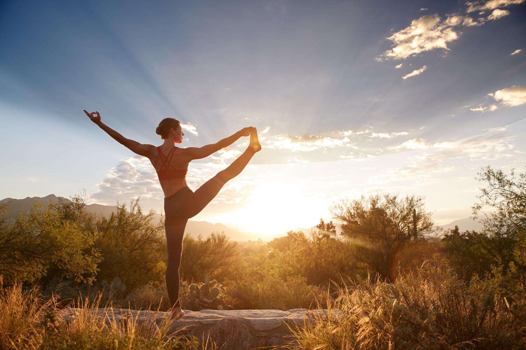 woman doing yoga on rock wall while the sun rises in the Sonoran Desert