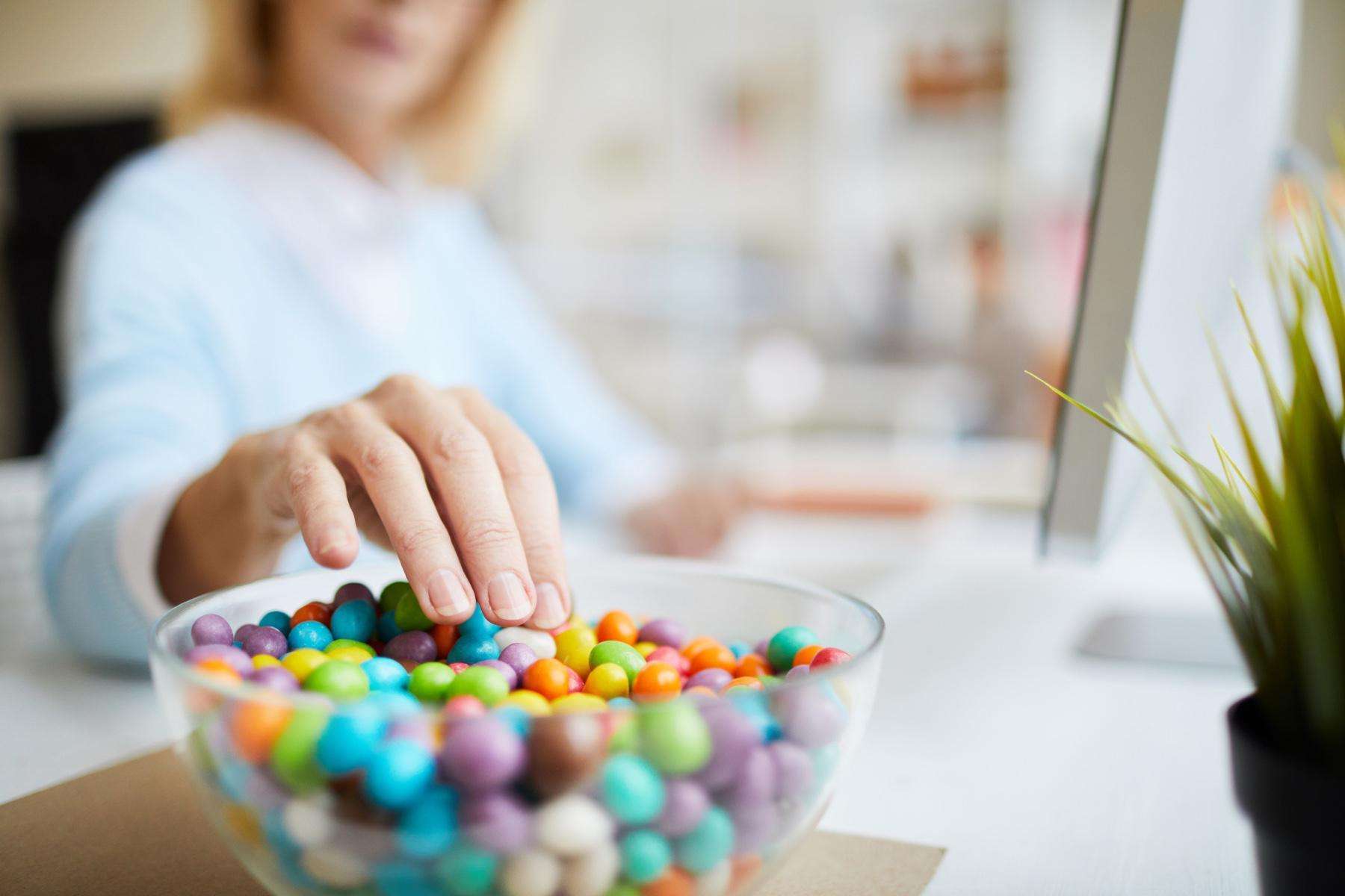 Close-up of woman sticking hand into bowl of candy.