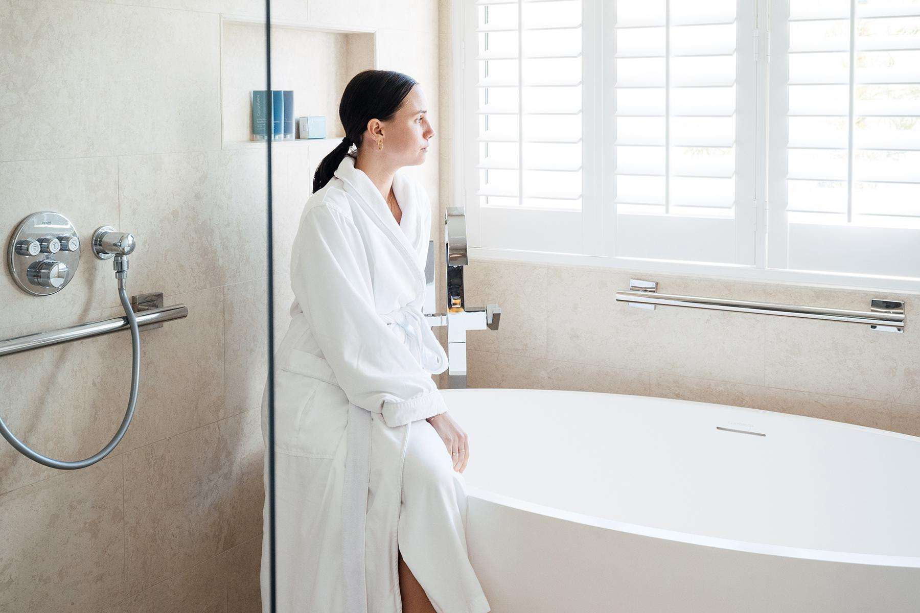 A woman standing in a Canyon Ranch Tucson suite bathroom next to the bathtub.