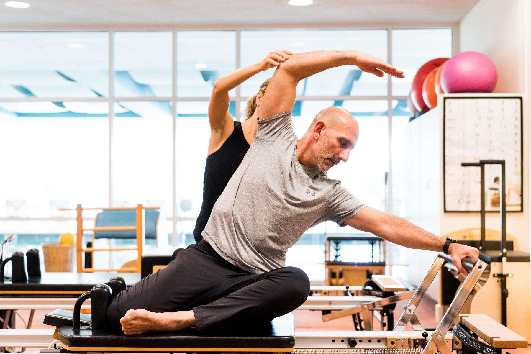 man being guided on pilates reformer machine by woman behind him