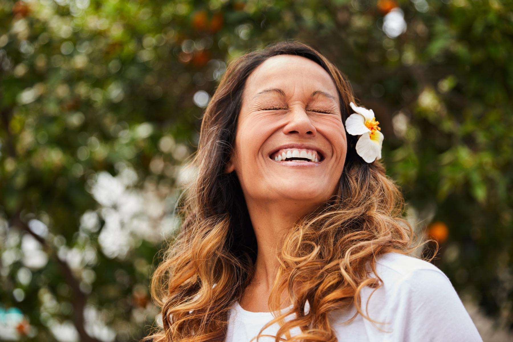 A woman with her eyes closed smiling with a flower tucked behind her ear.