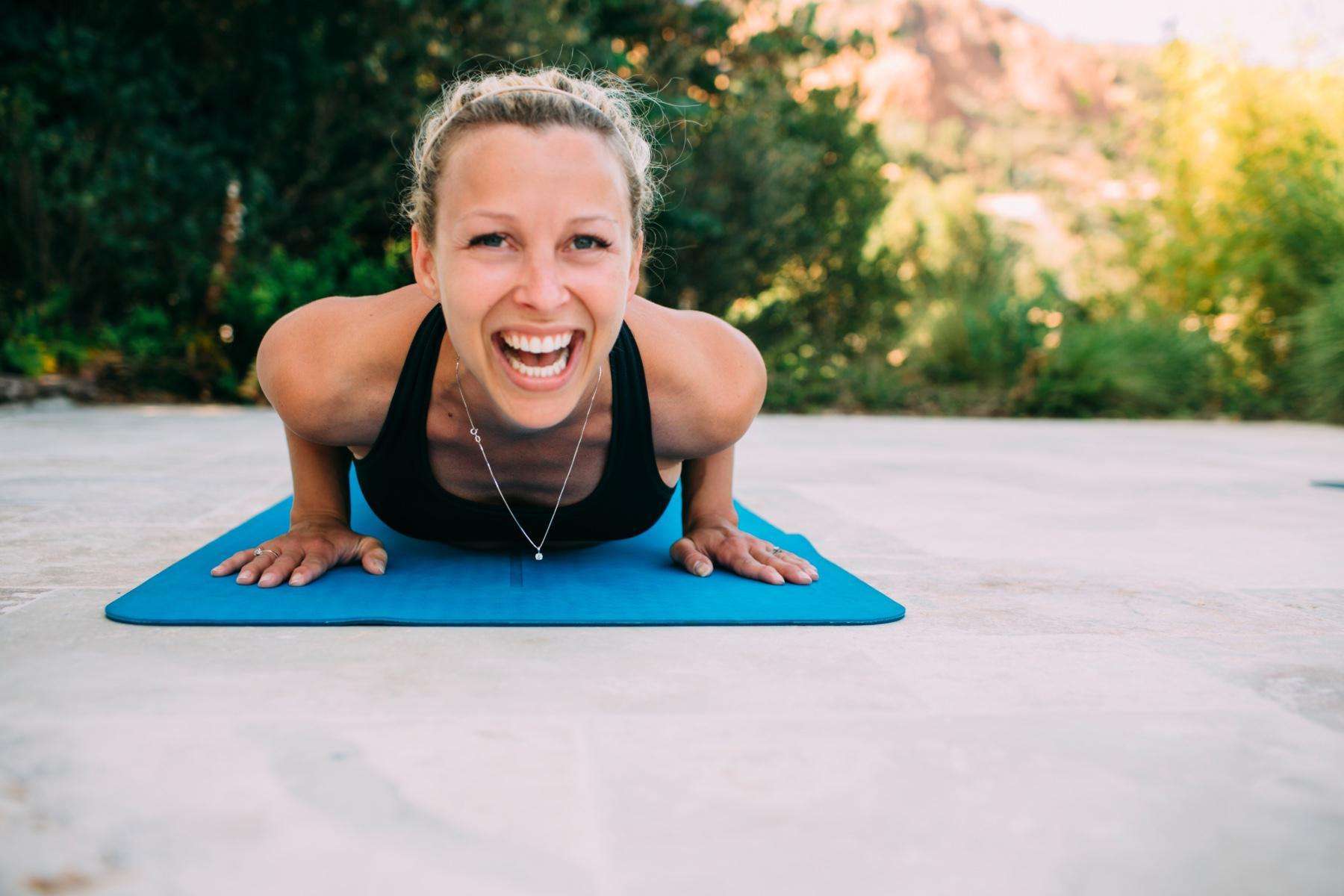 close-up of woman's face as she laughs while laying on yoga mat outside