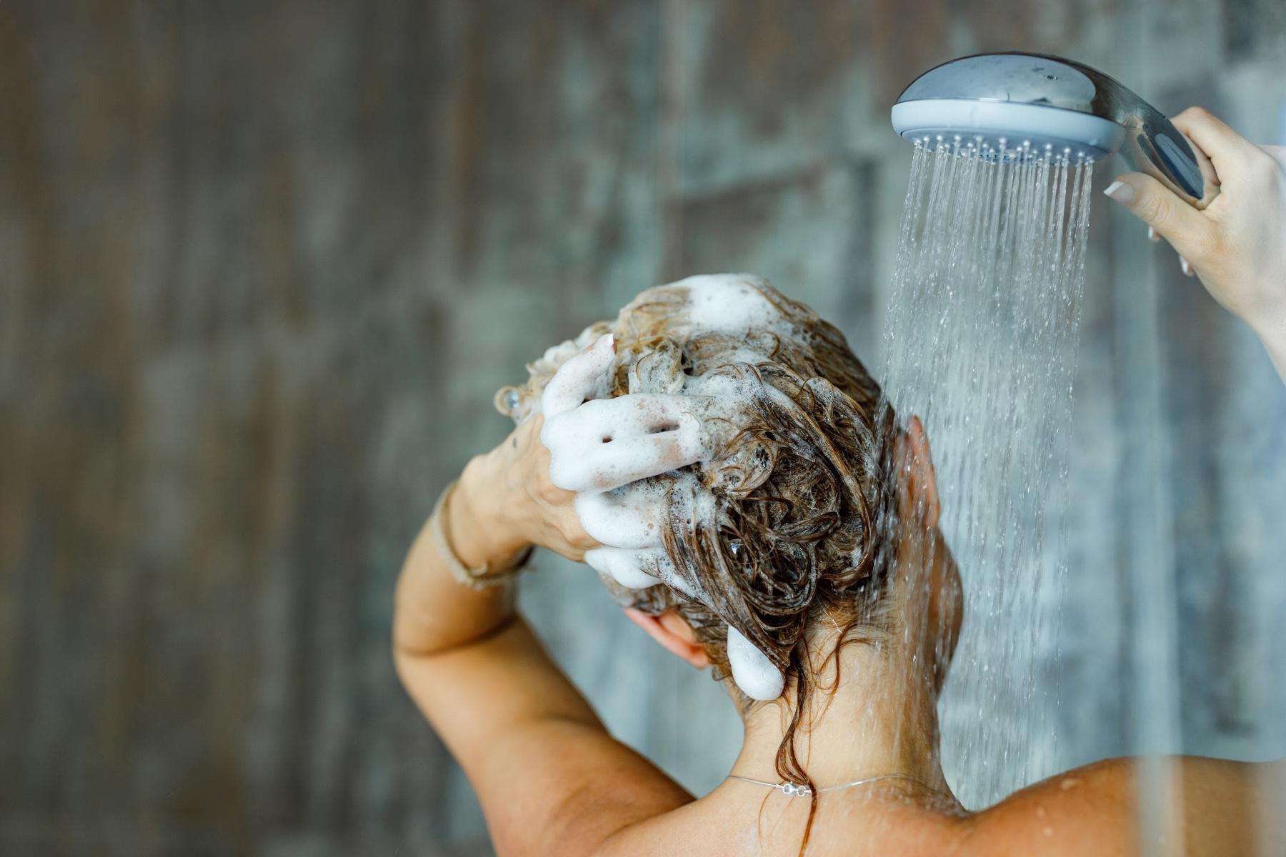 A woman washing her hair with shampoo in the shower.