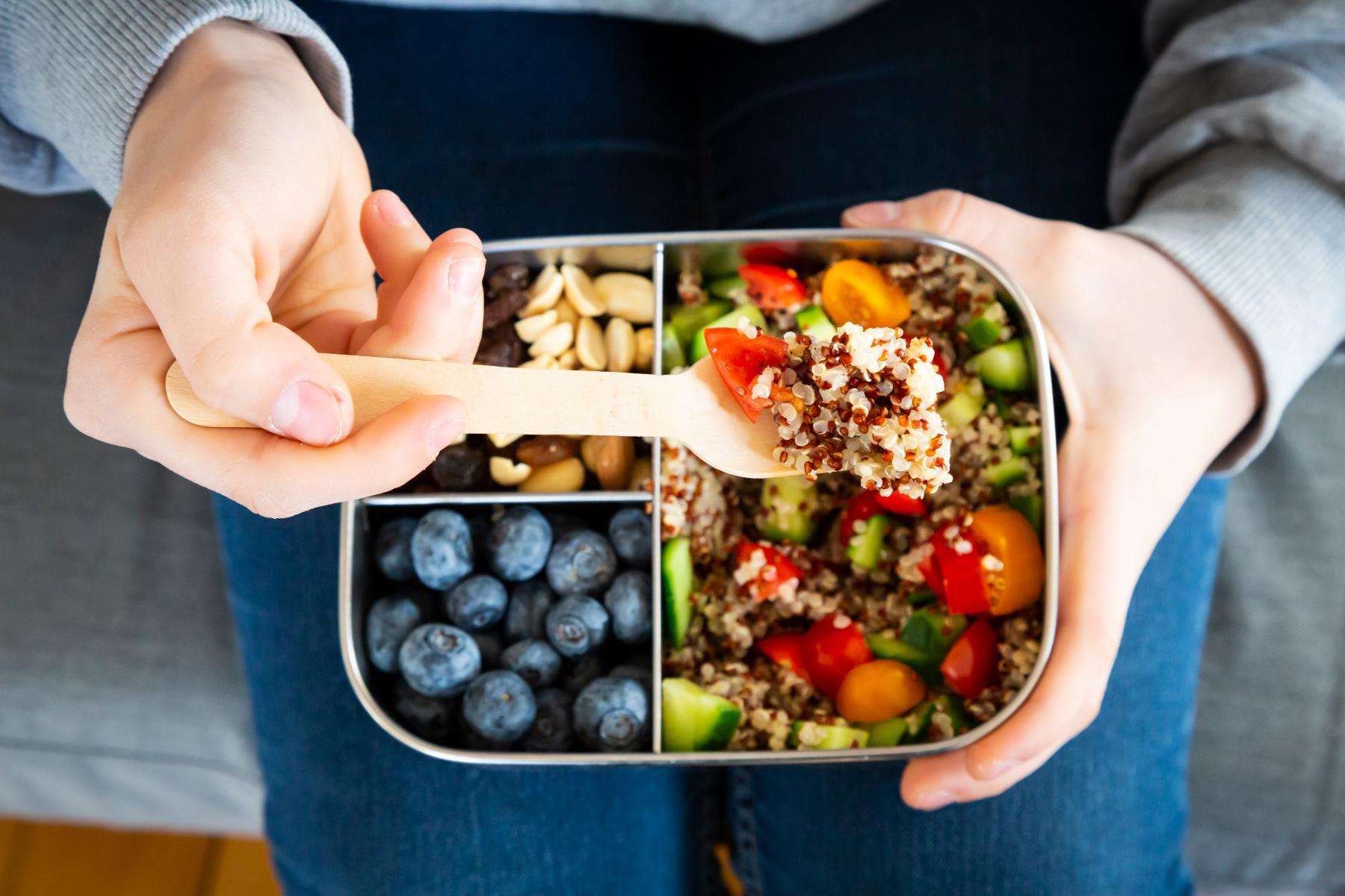 Close-up of hand spooning quinoa out of metal lunch tin.