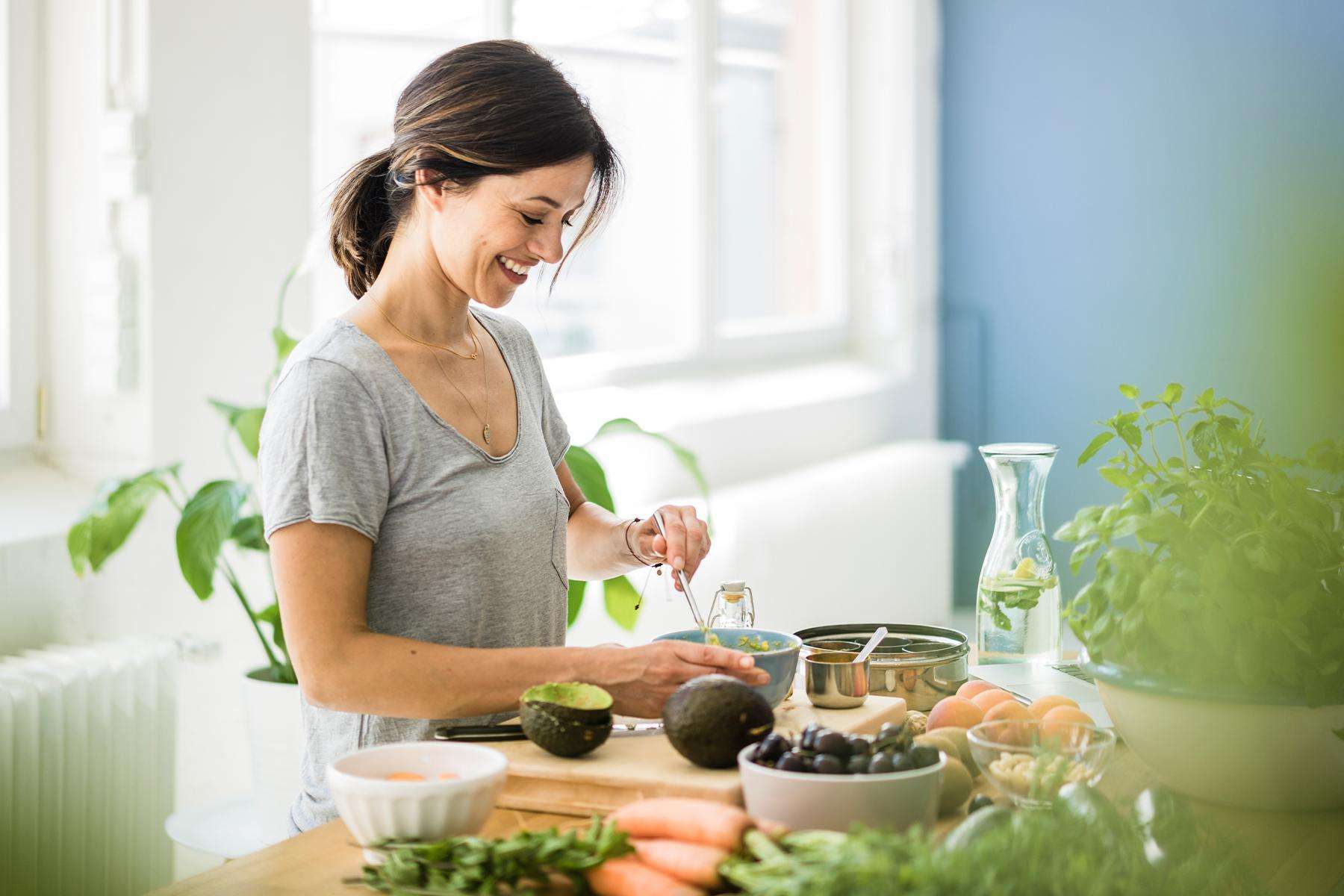 woman smiling from size while making guacamole in bright kitchen
