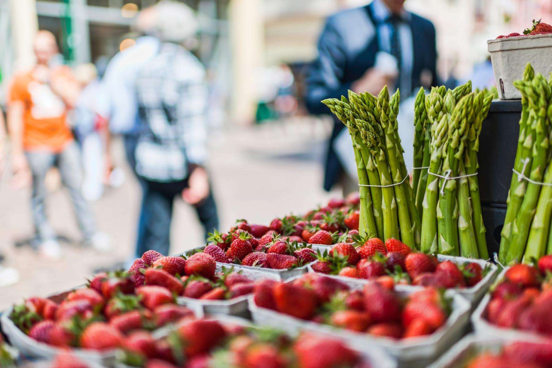 Close-up image of fresh strawberries and asparagus on a table at a farmer's market.