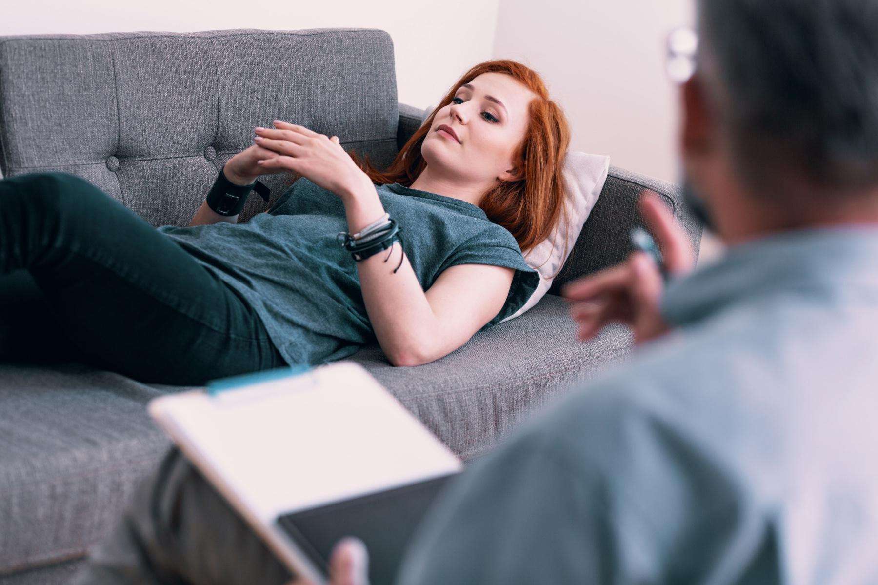 A woman lying on a couch while speaking with her therapist.