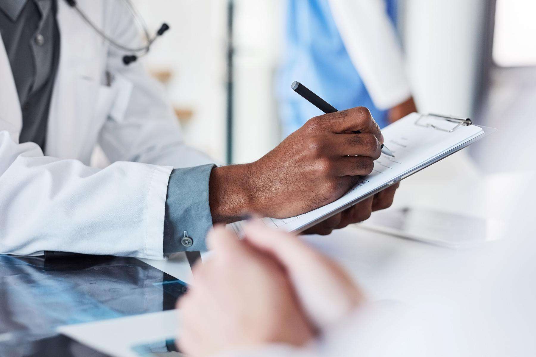 Close-up of doctor's hand writing on clipboard with pen.
