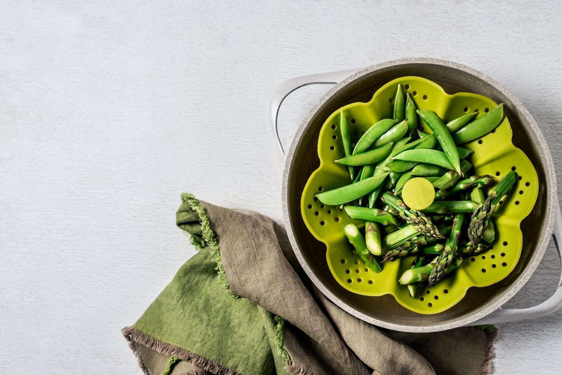 Overhead view of peas in a green vegetable steamer.