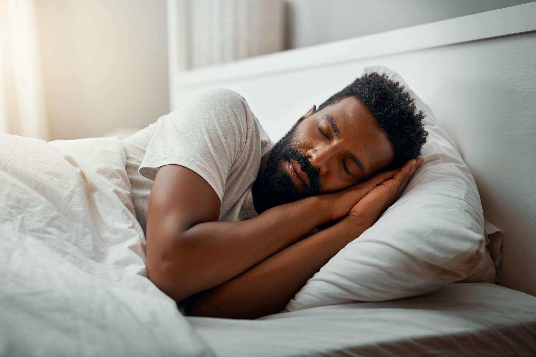 Man laying on his side in a bed with hands tucked up under the side of face.