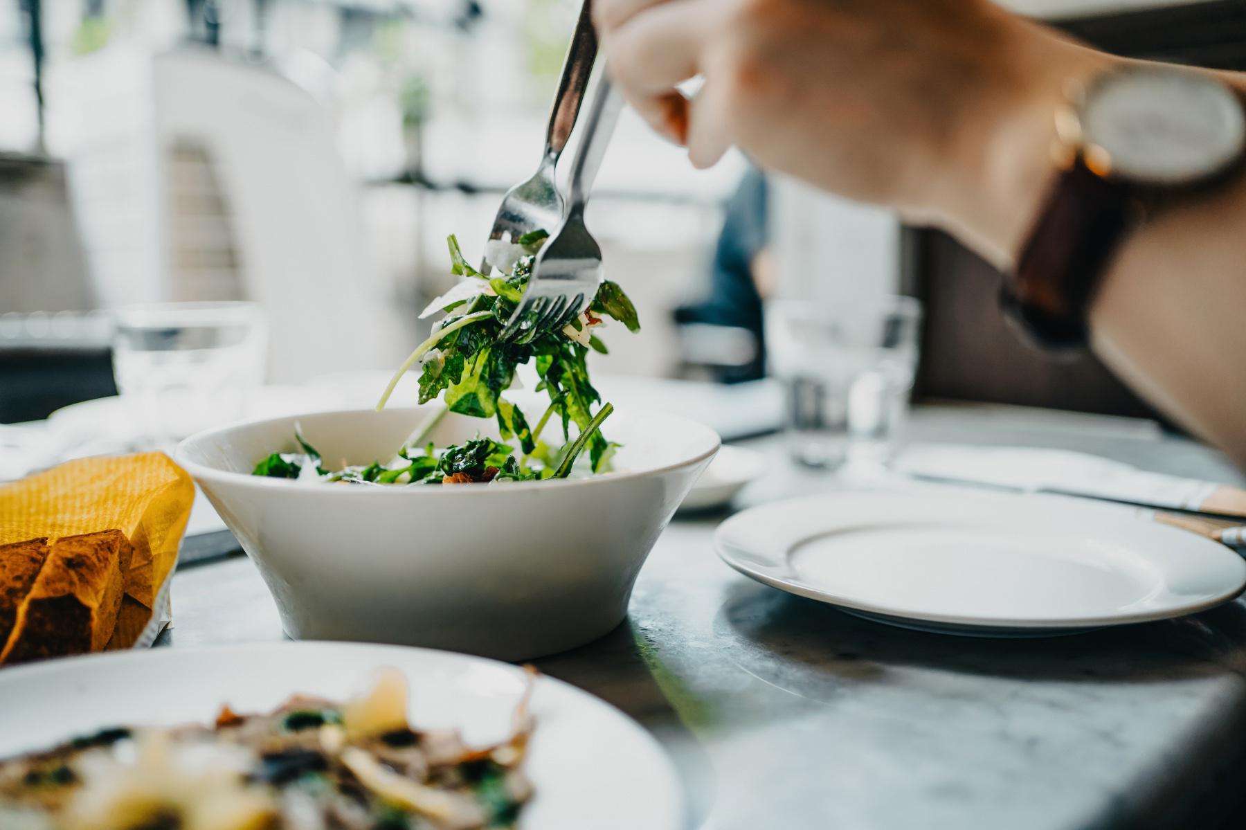 A man using two forks to pick up lettuce from a small bowl.