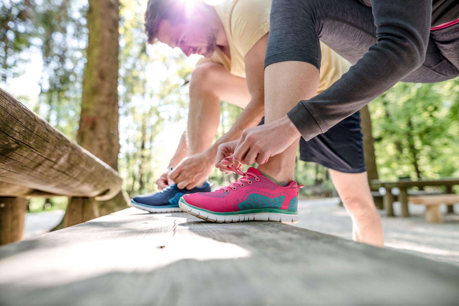 Close-up of man and women tying their shoes on a bench.