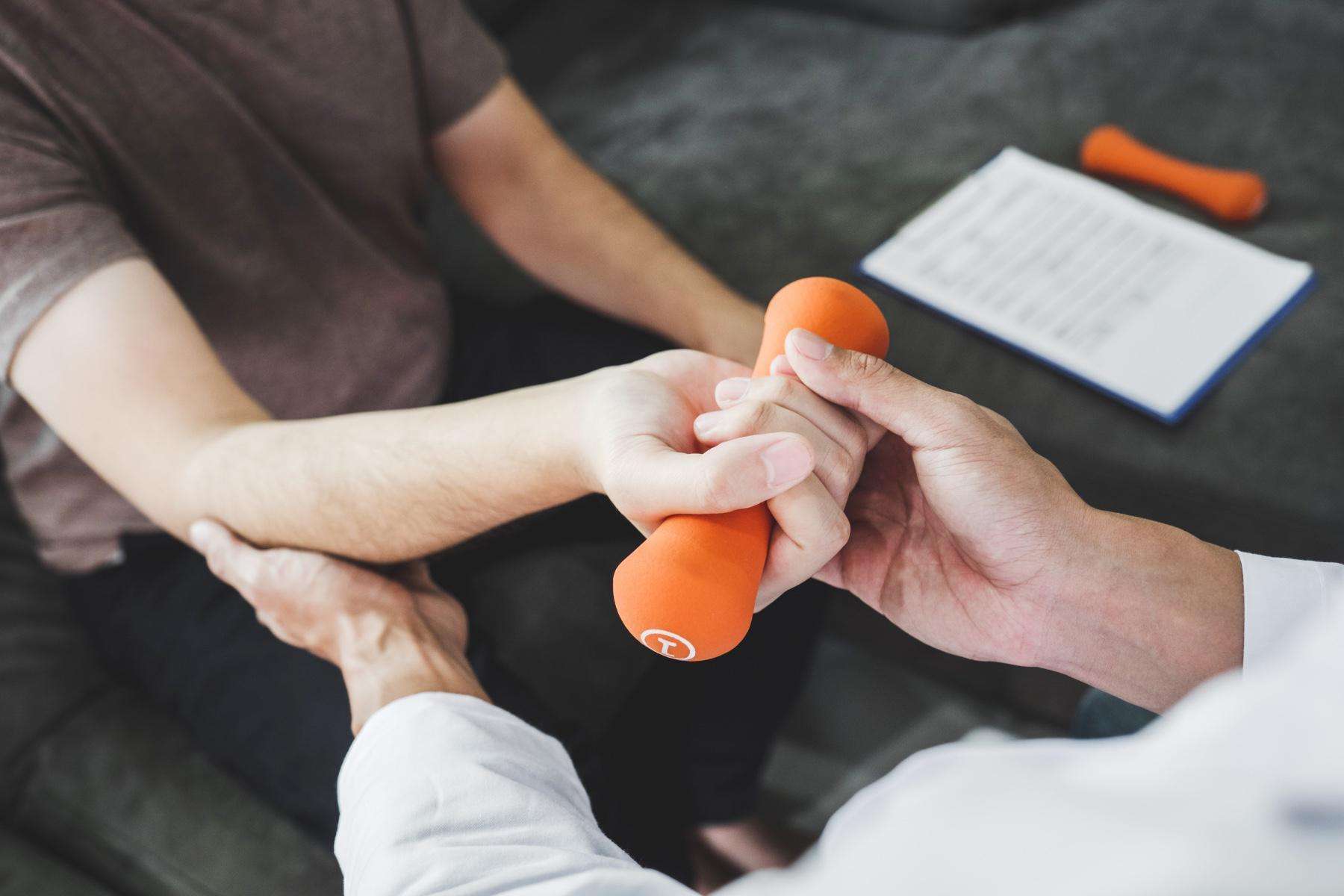 Close-up on man receiving assistance from a physical therapist as he curls a 1 pound orange dumbbell.