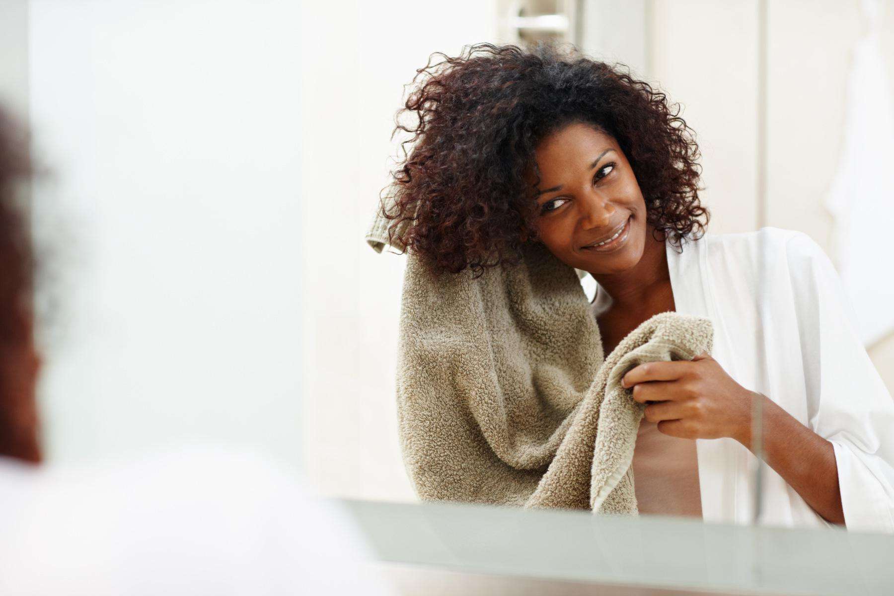 A young woman drying her curly hair with an olive green colored towel.
