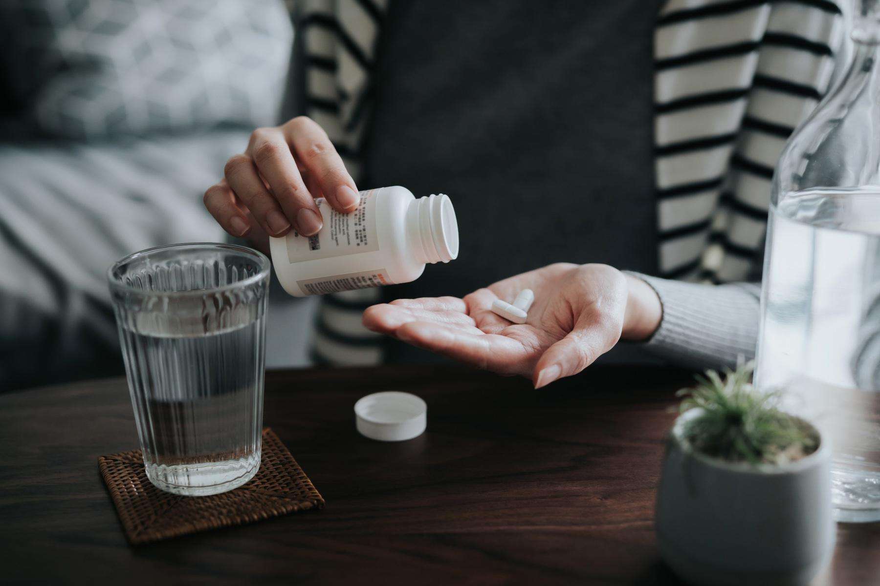 Close-up of woman pouring supplements out of bottle into her hand.