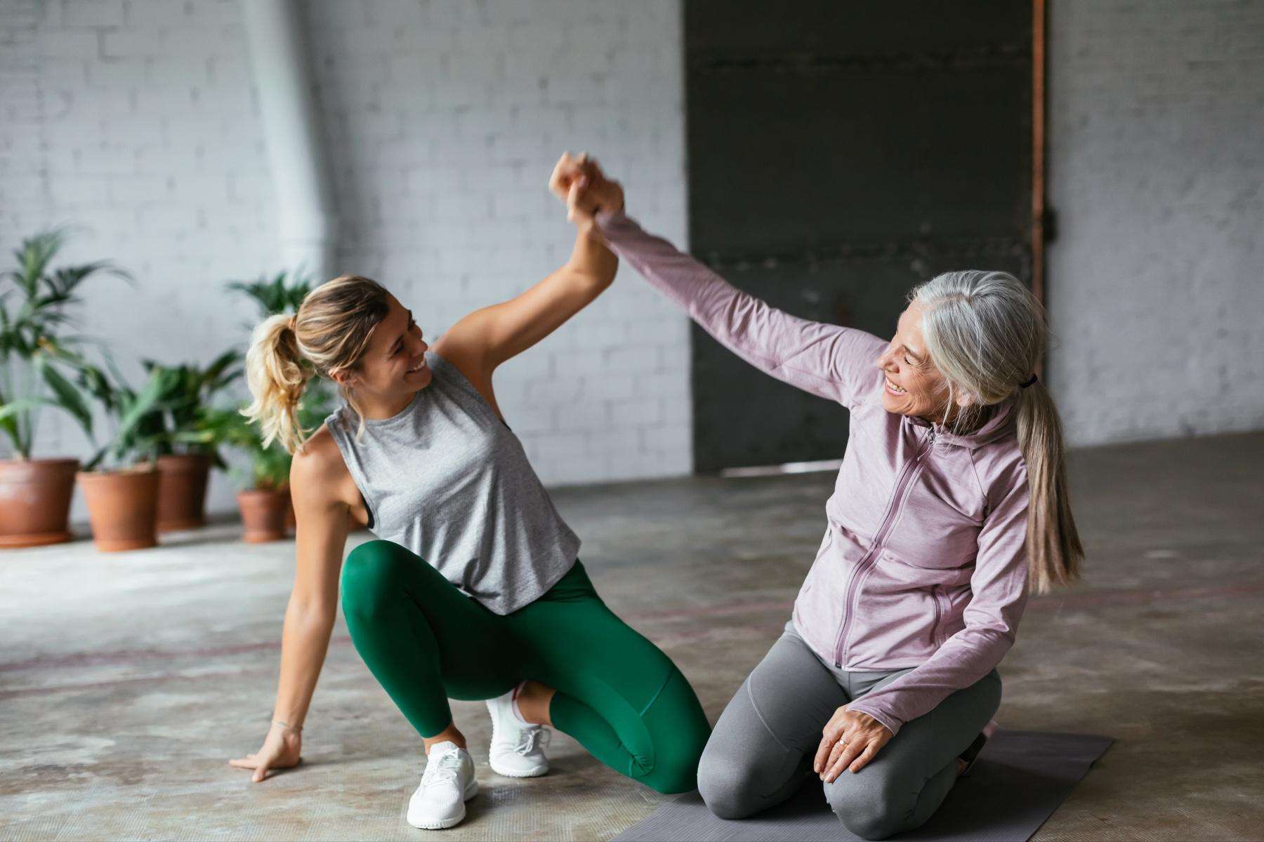two women mid workout kneeling on the ground and holding their hands together in the air in celebration
