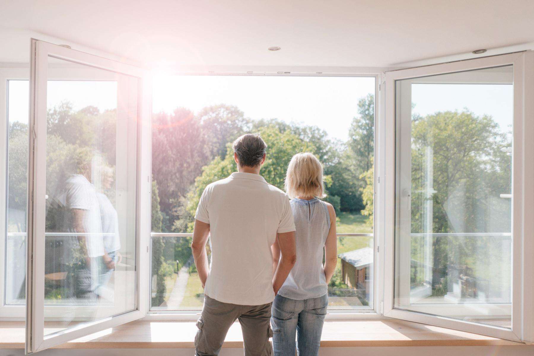 A couple looking outside of a large window at trees.
