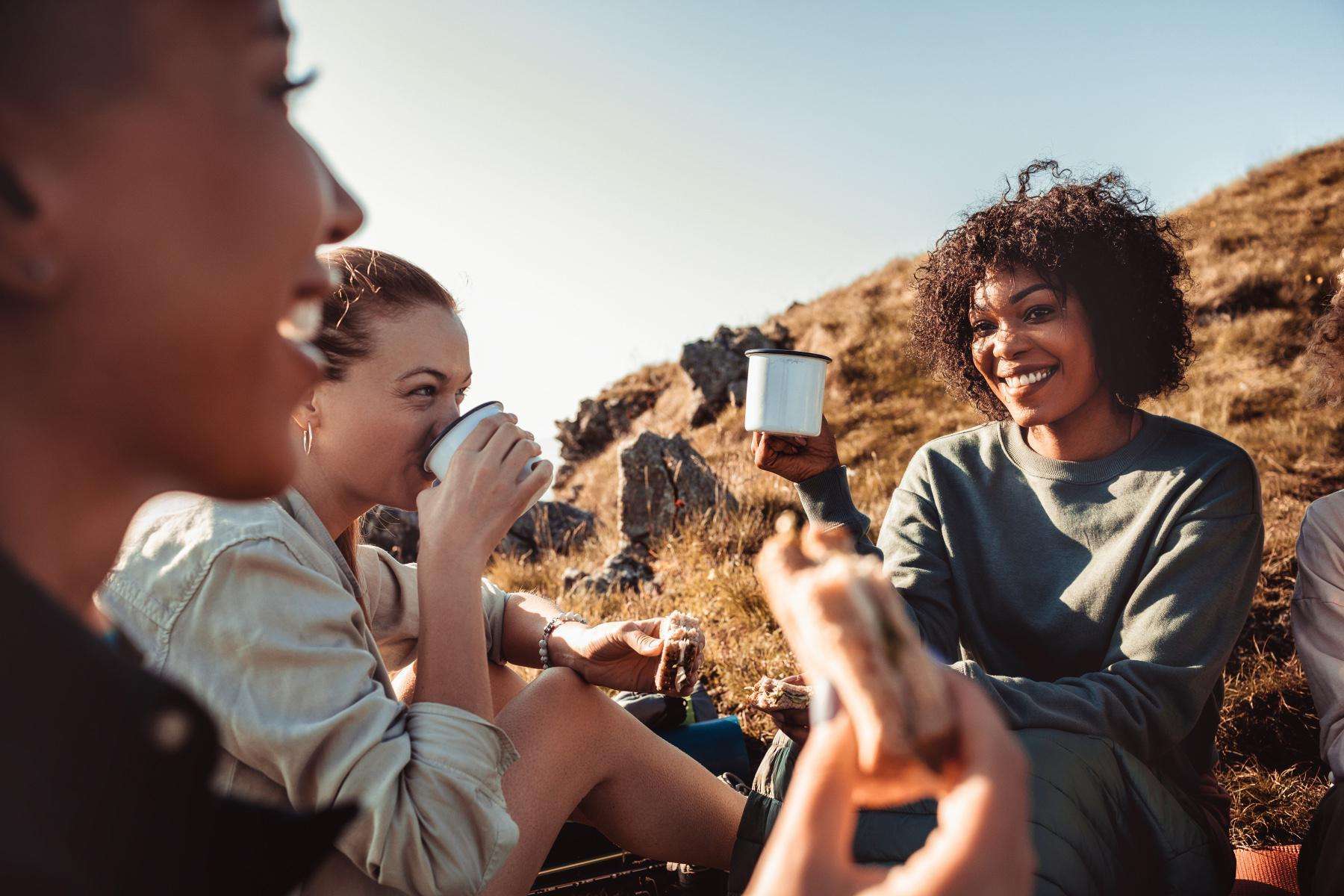 Three women sitting on mountain top drinking coffee.