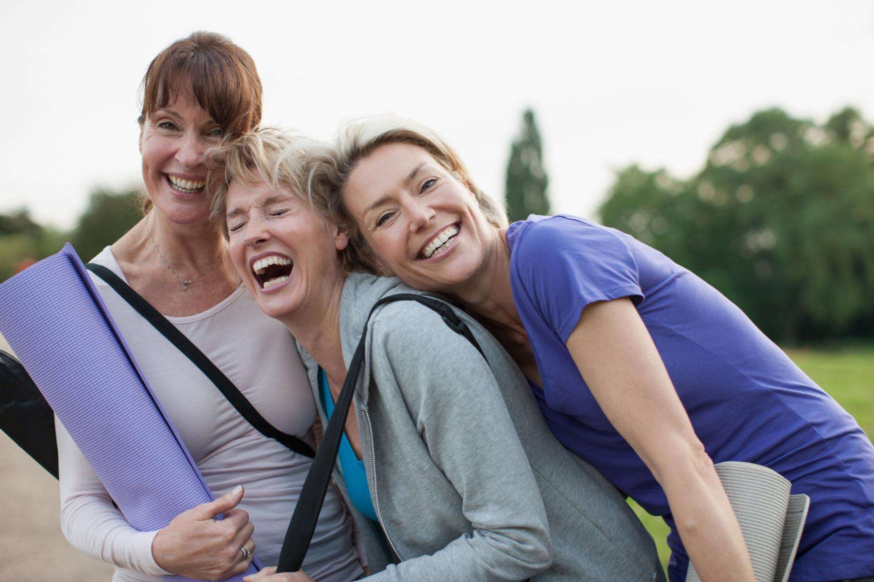Group of three happy, older woman laughing and smiling together outside.