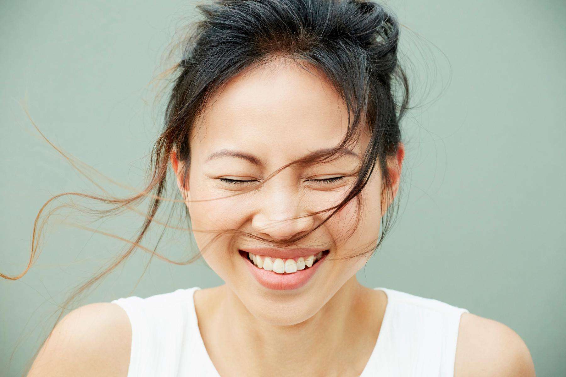 A close-up of a woman smiling with her eyes closed as the wind blows her hair into her face.
